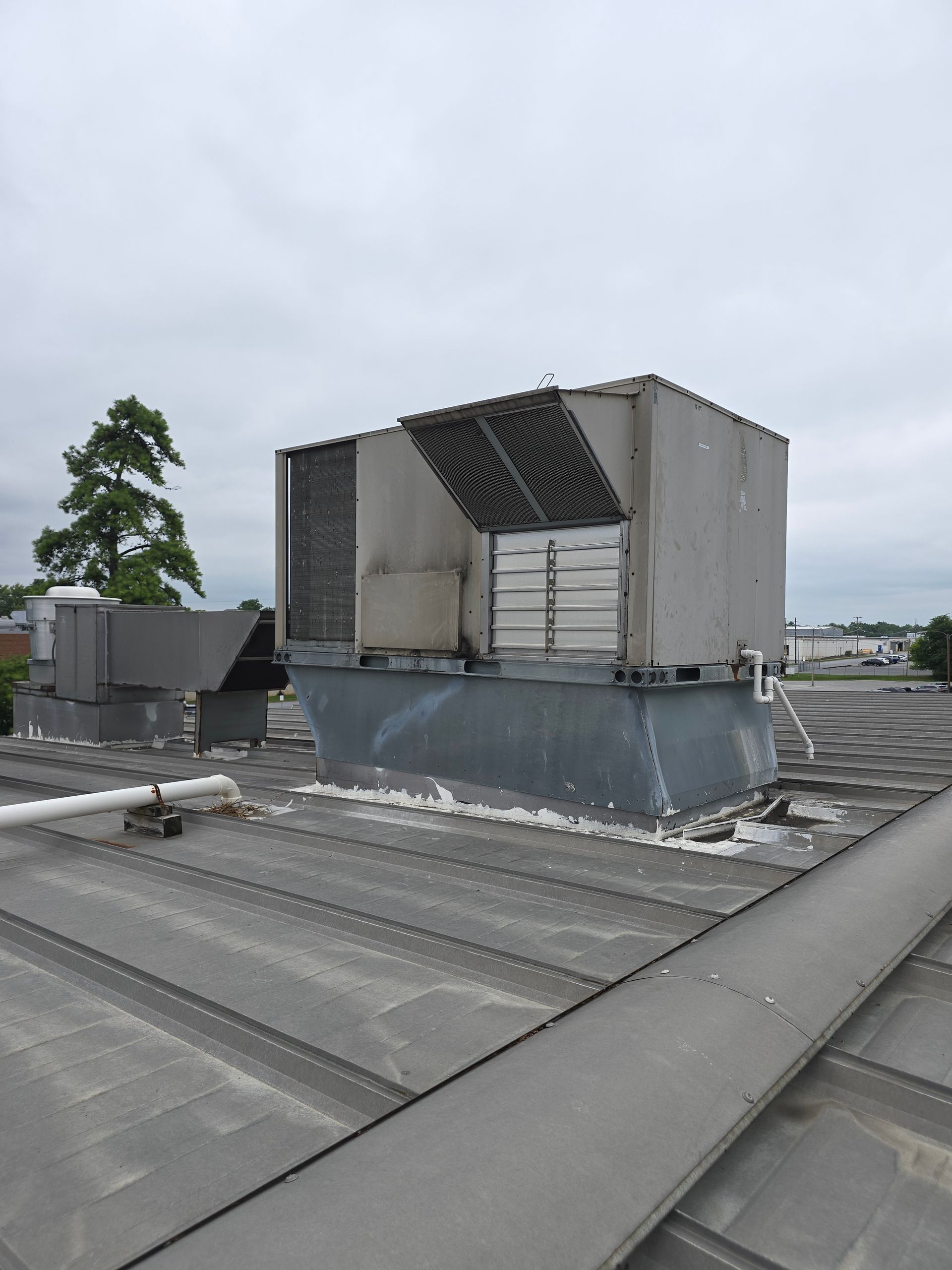 Rooftop HVAC unit with metal ductwork and vents on a flat industrial roof under cloudy sky