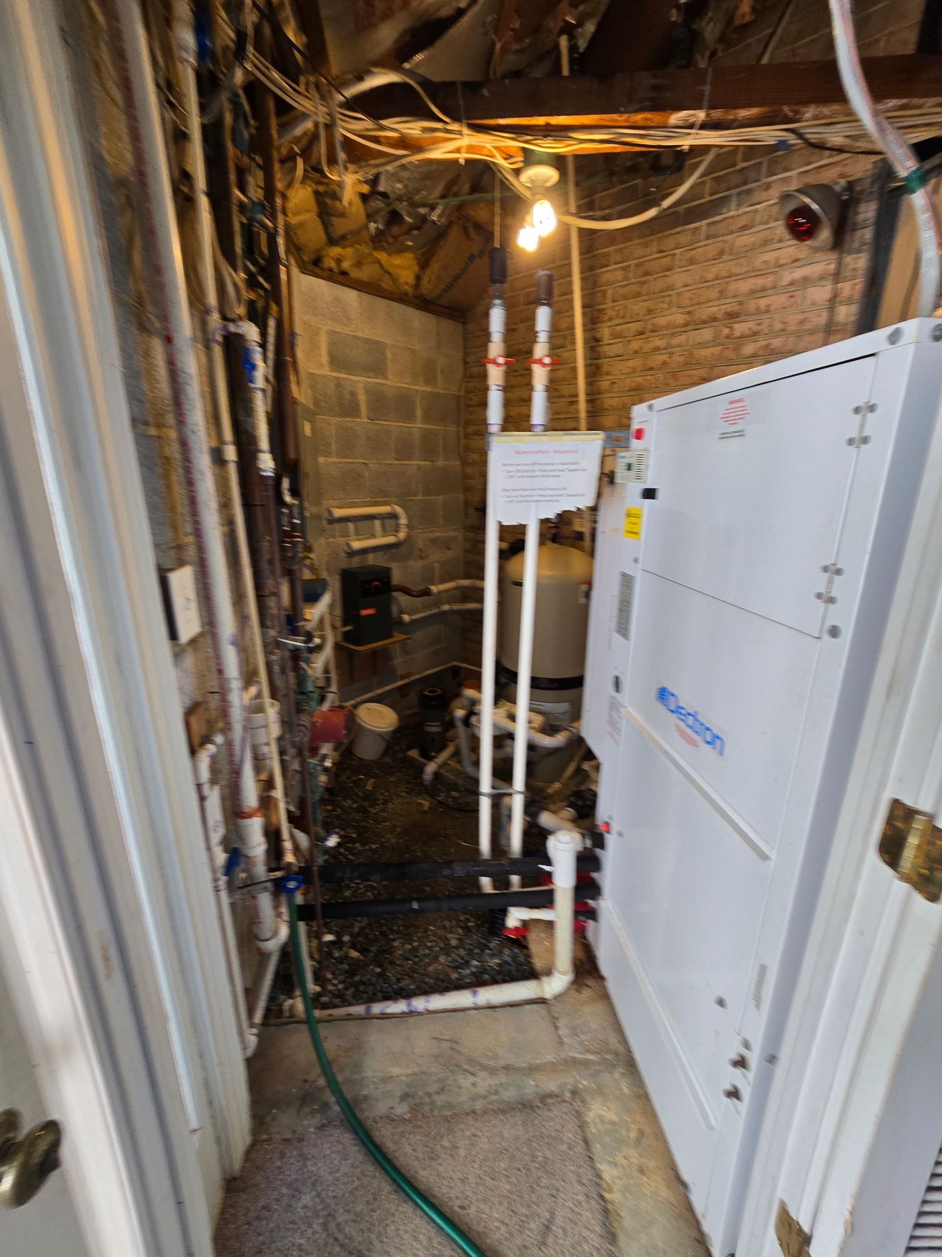 Utility room with exposed pipes, boiler equipment, and a white cabinet in a narrow basement space.