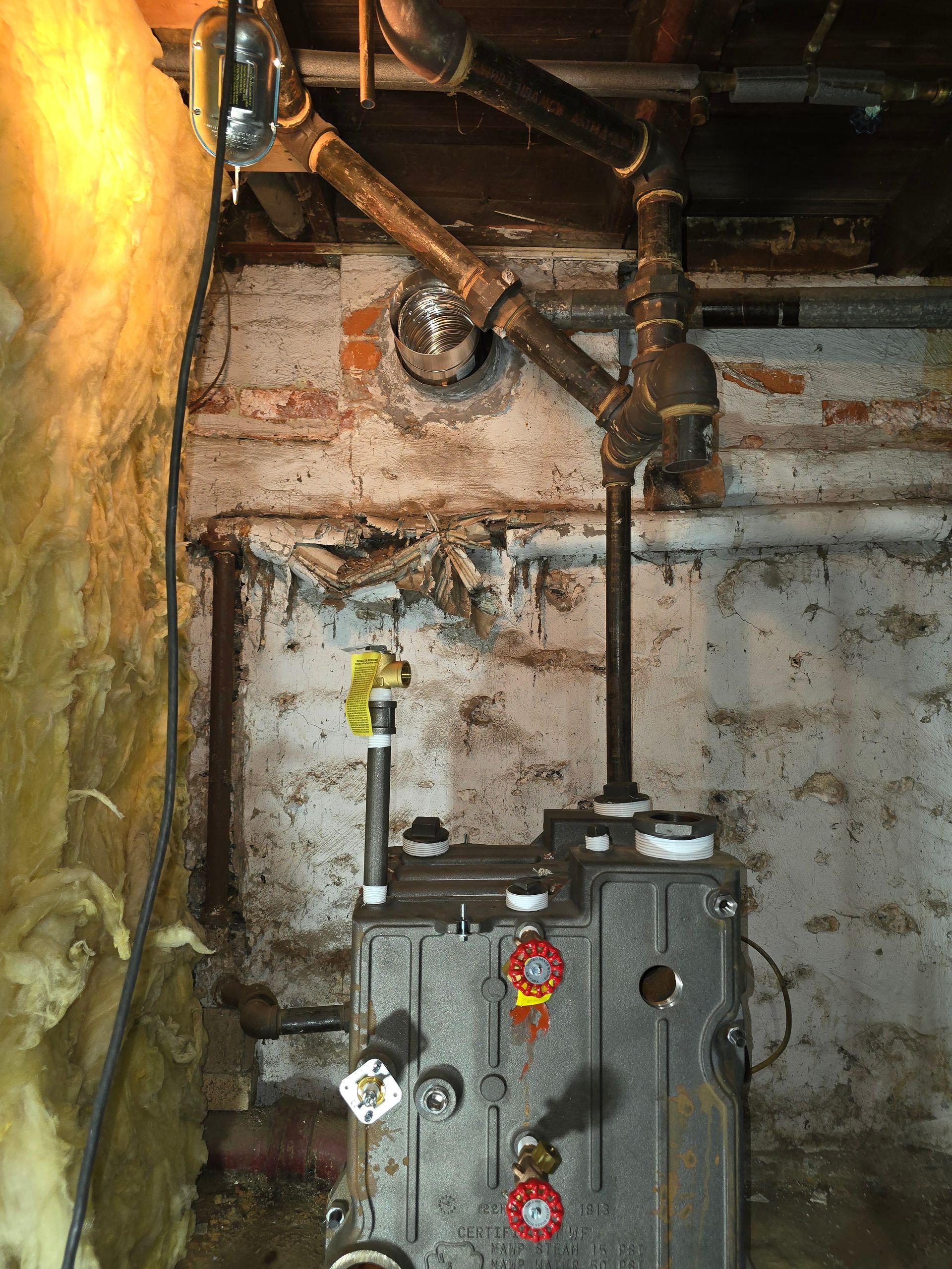 Basement utility room with exposed pipes, wall-mounted valves, and a gray mechanical unit.