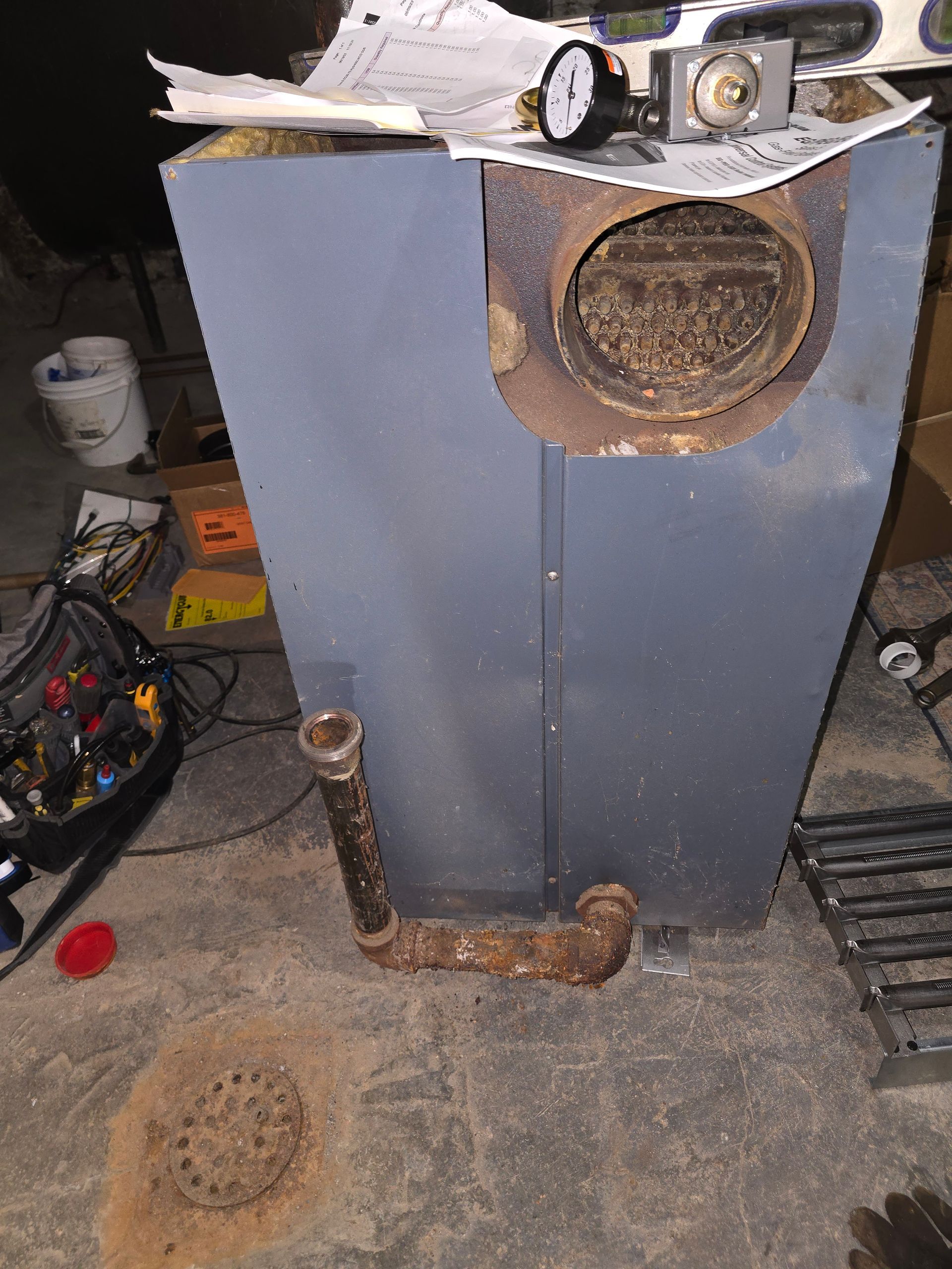 Rusty metal cabinet with round openings and tools on top in a cluttered workshop area