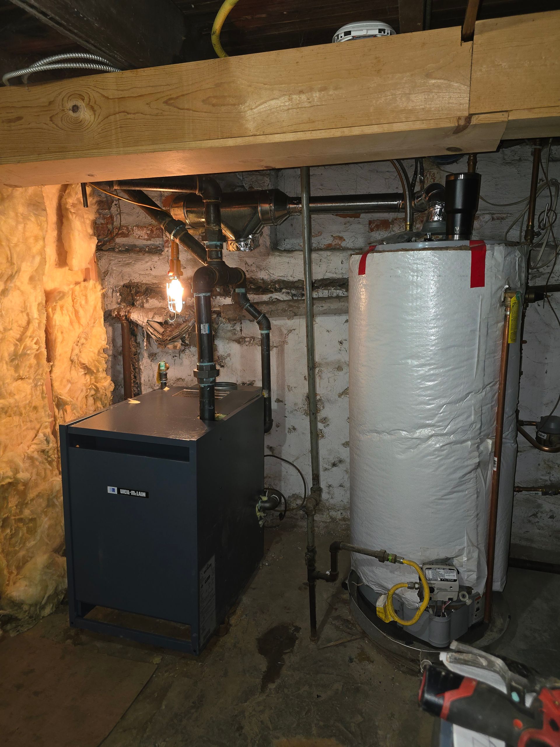 Basement with a furnace, water heater, exposed pipes, and insulation under low ceiling joists