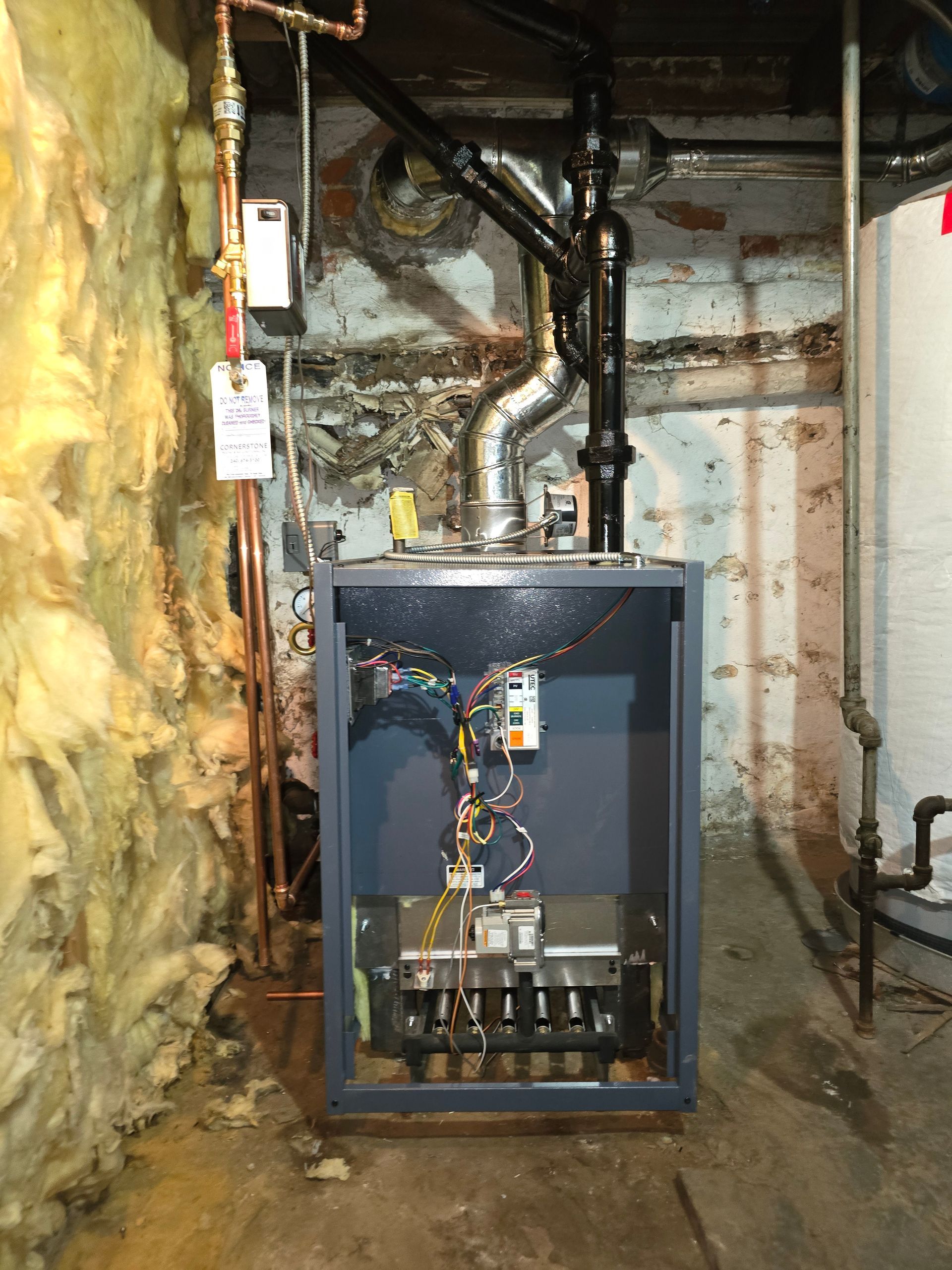 Open furnace in unfinished basement with exposed pipes, wiring, and insulation beside it