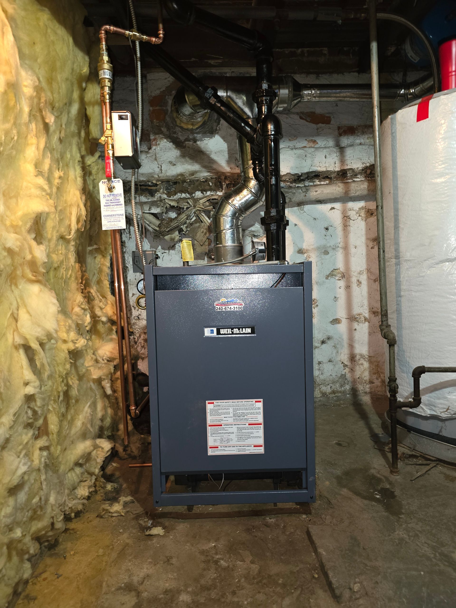 Basement utility room with a gray furnace, exposed pipes, and insulation along the wall.