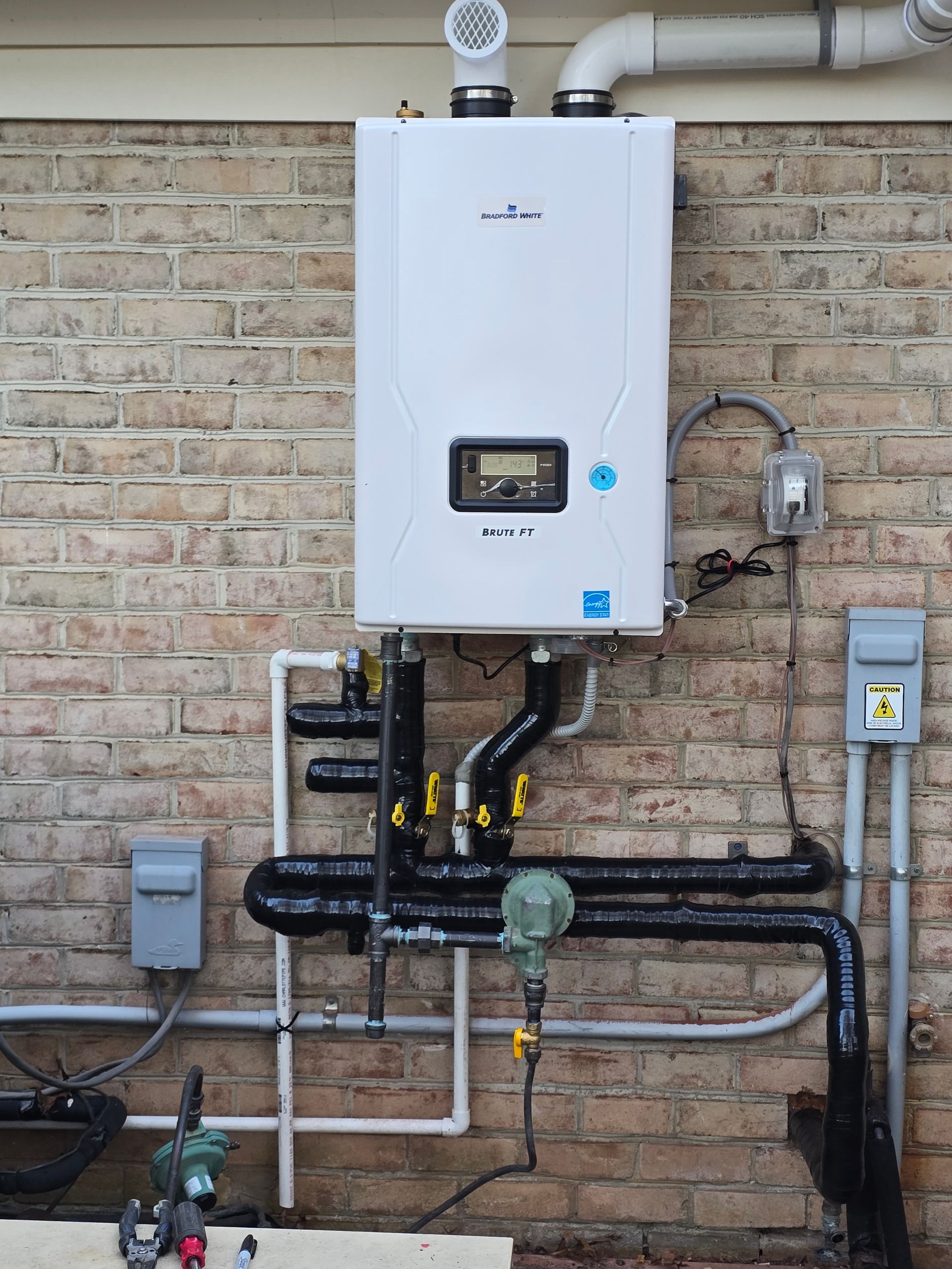 Wall-mounted white boiler with pipes and gauges on an exterior brick wall