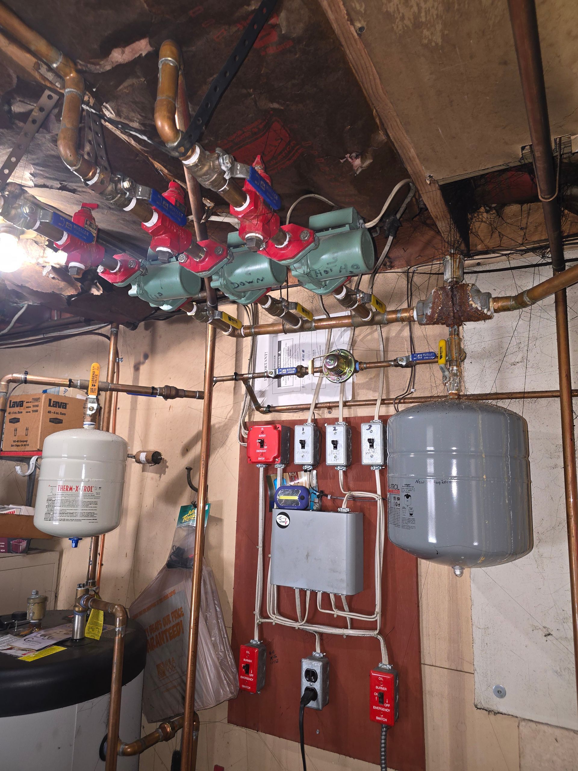 Basement utility area with pipes, valves, electrical panels, and two gray water tanks on unfinished walls
