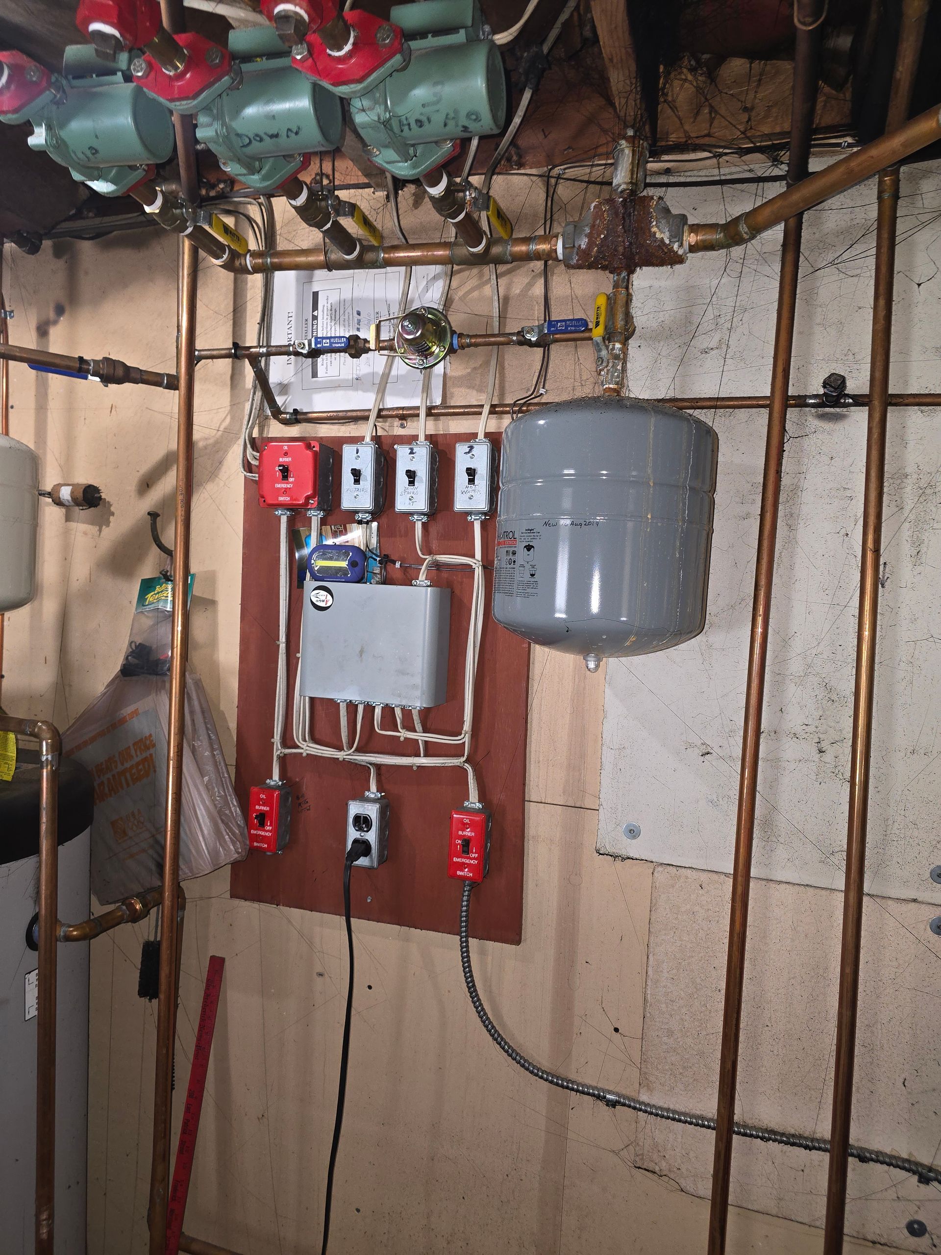 Basement wall with electrical panel, meters, red wires, and a gray water heater tank.