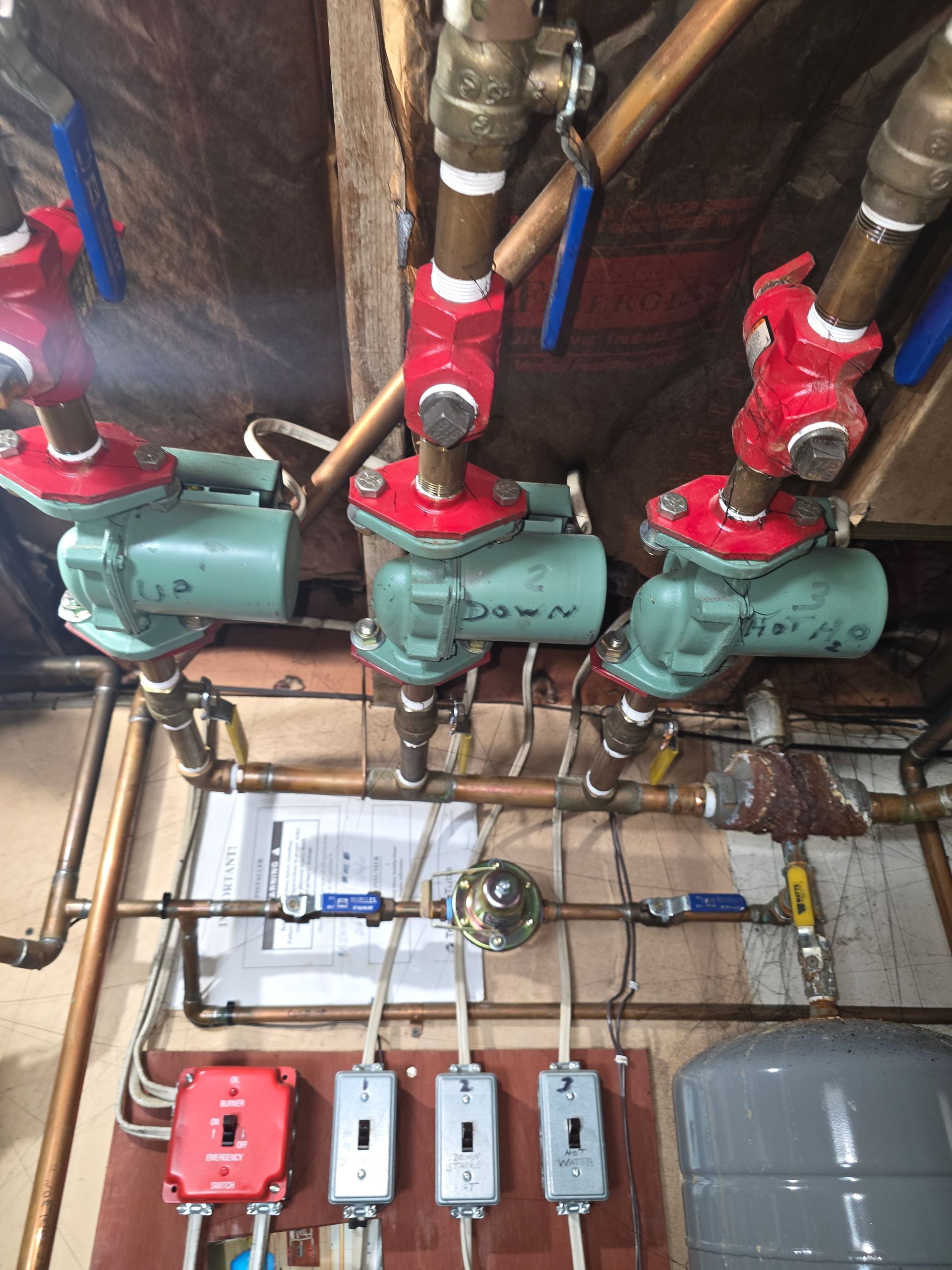 Three green water pumps with red valves and pipes in an industrial basement, with electrical boxes below