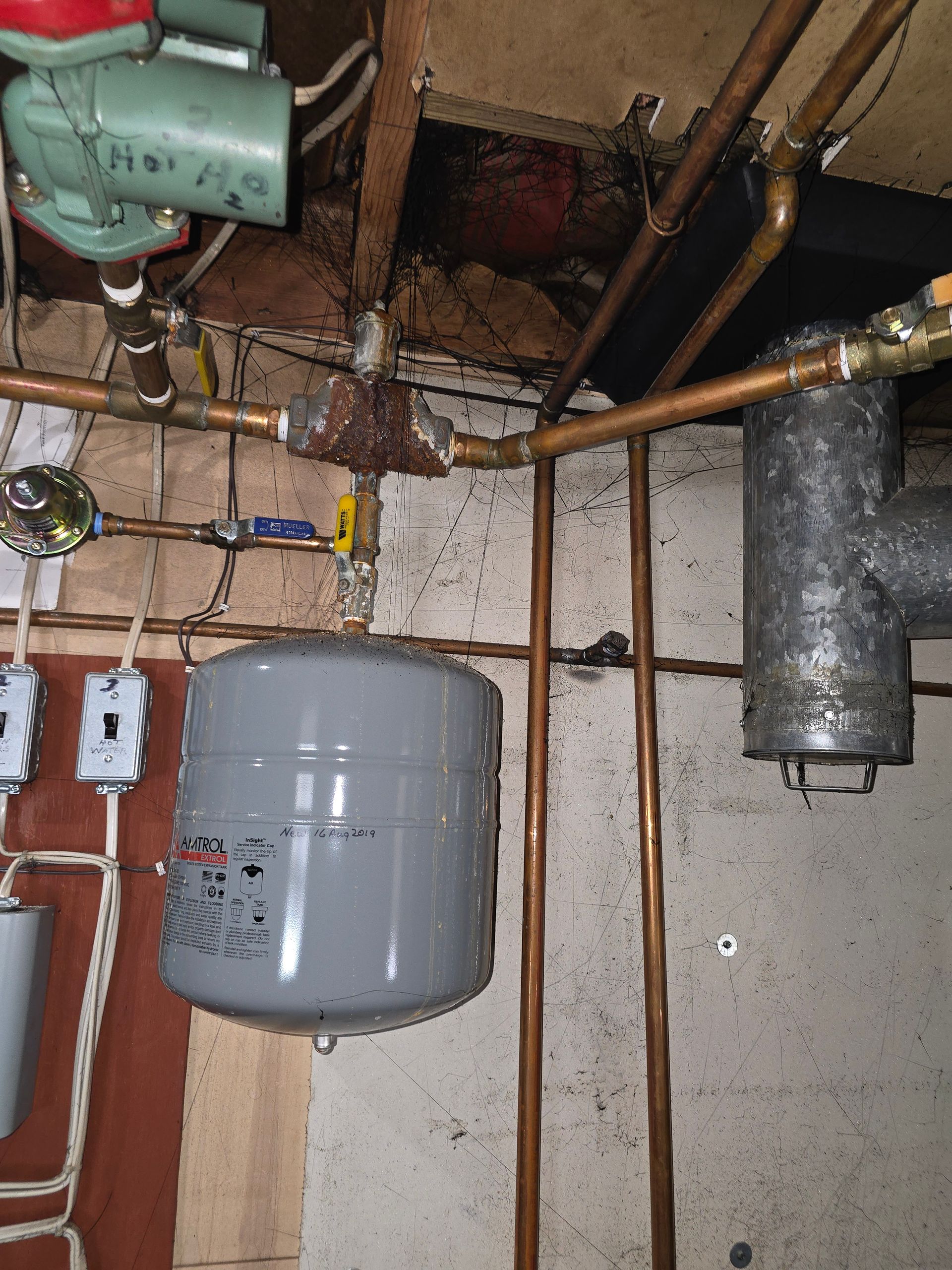 Basement utility area with exposed pipes, a gray tank, and electrical wiring on a concrete wall.