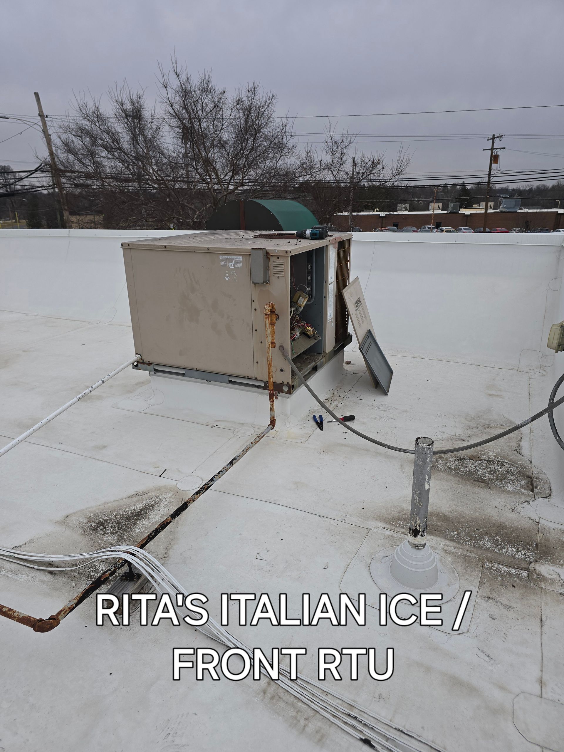 Damaged rooftop HVAC unit with bent panel and debris on snowy white roof under overcast sky