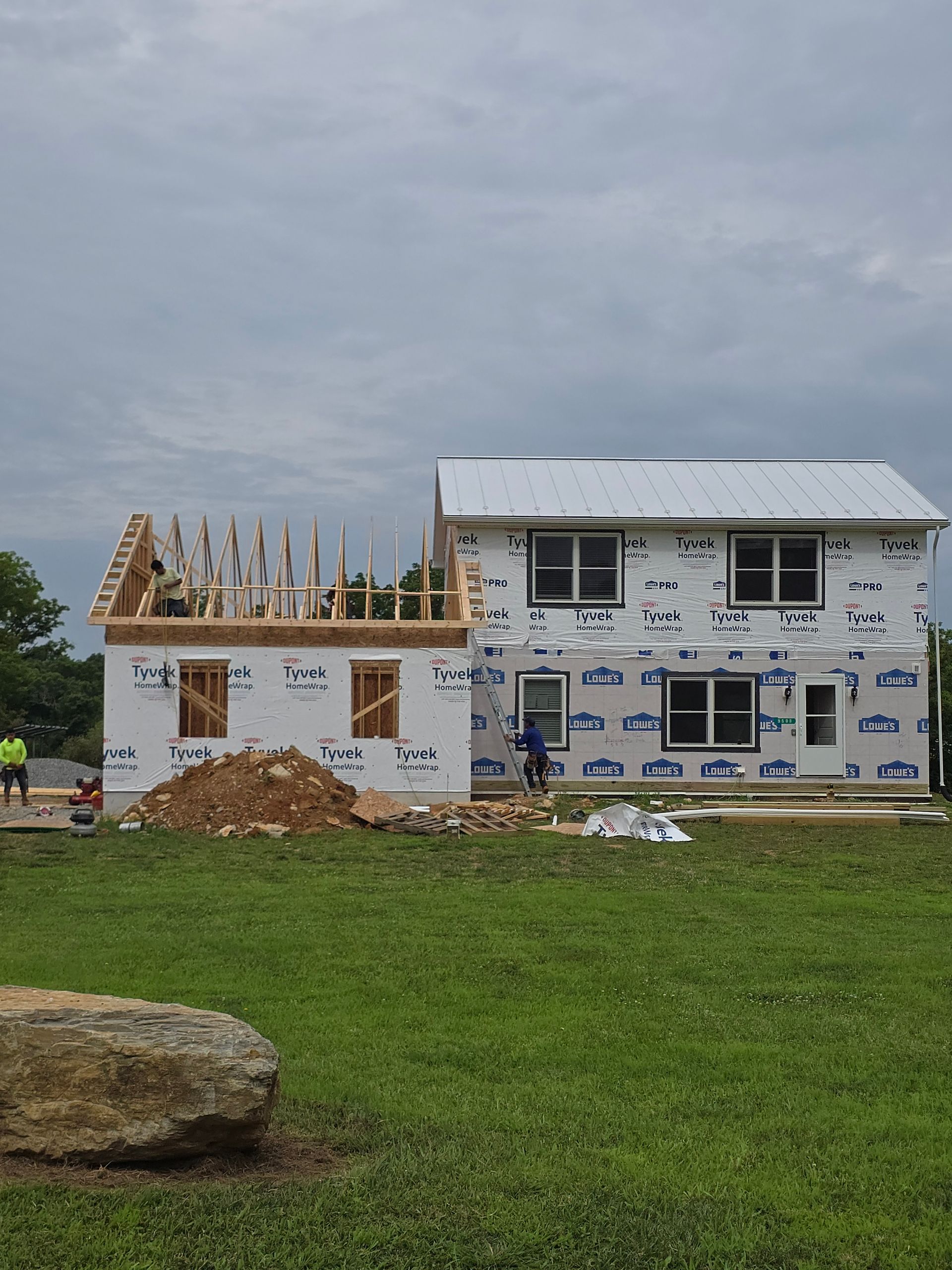 Two-story house under construction with exposed framing, white siding, and a cloudy sky overhead