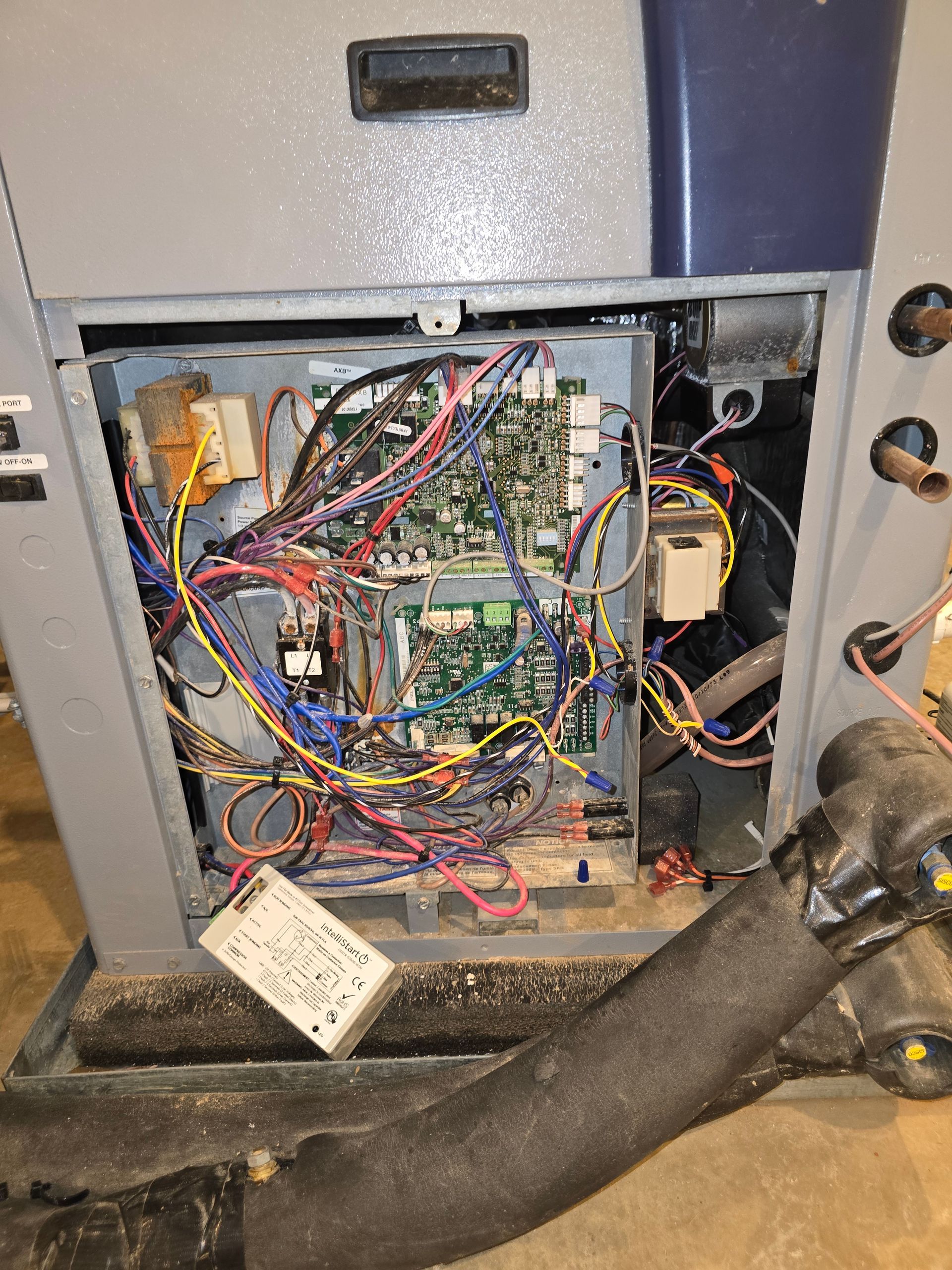 Open electrical control panel with exposed circuit boards, tangled wires, and a hanging connector.