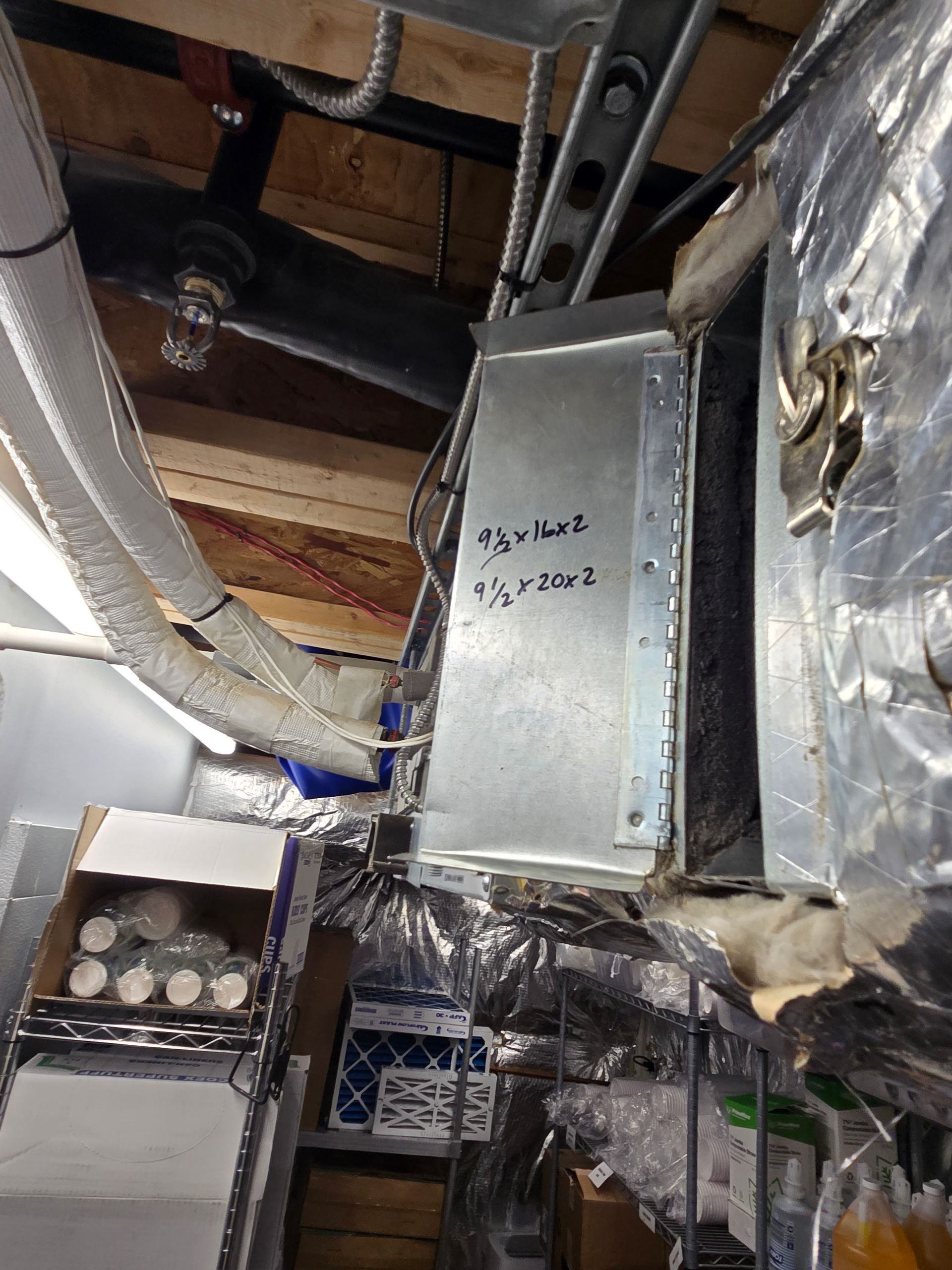 Insulated HVAC ducts and metal vent box in an unfinished attic ceiling.