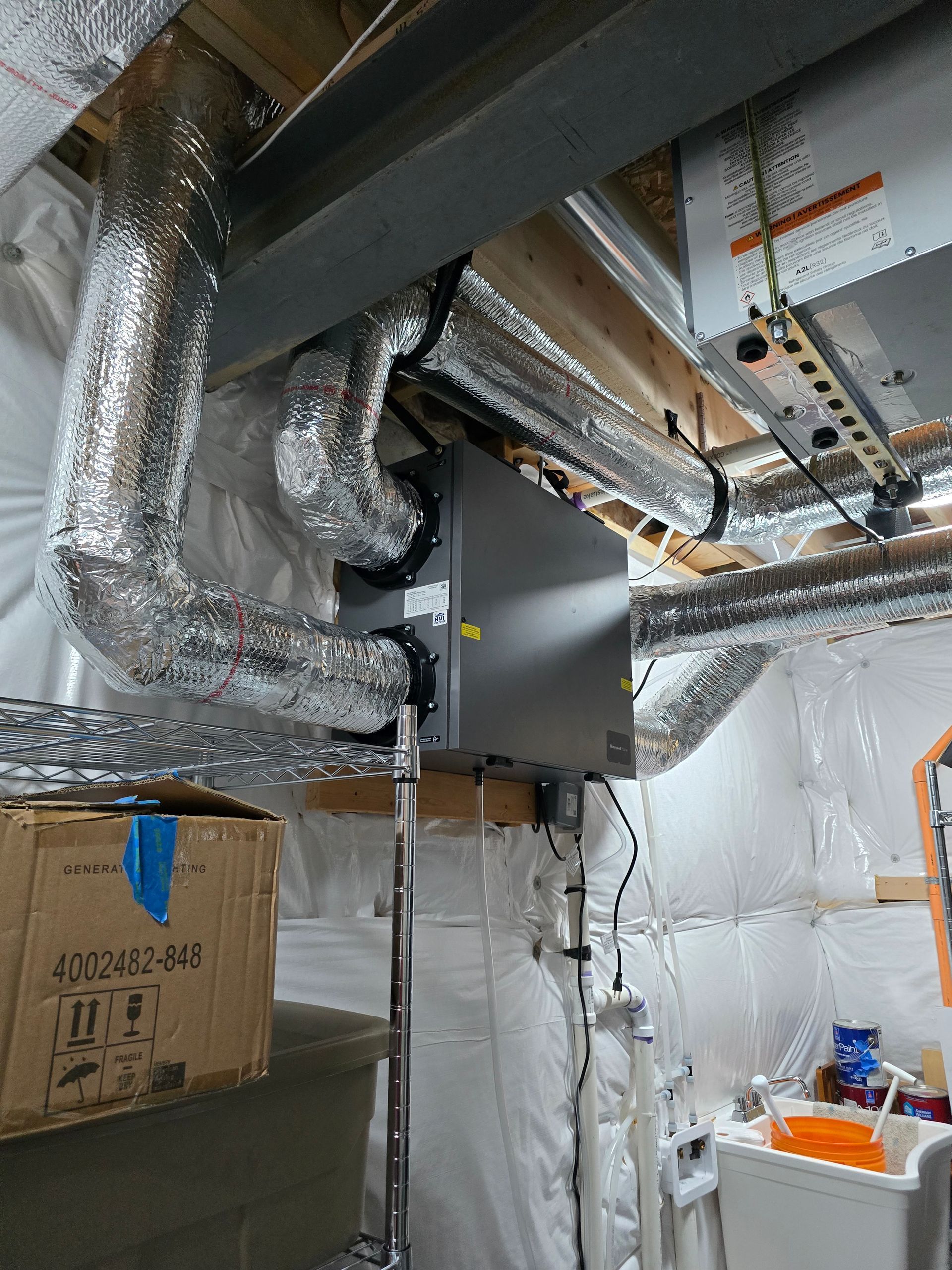 Insulated HVAC ducts and metal beams in an unfinished attic or crawlspace with boxes and a white panel below
