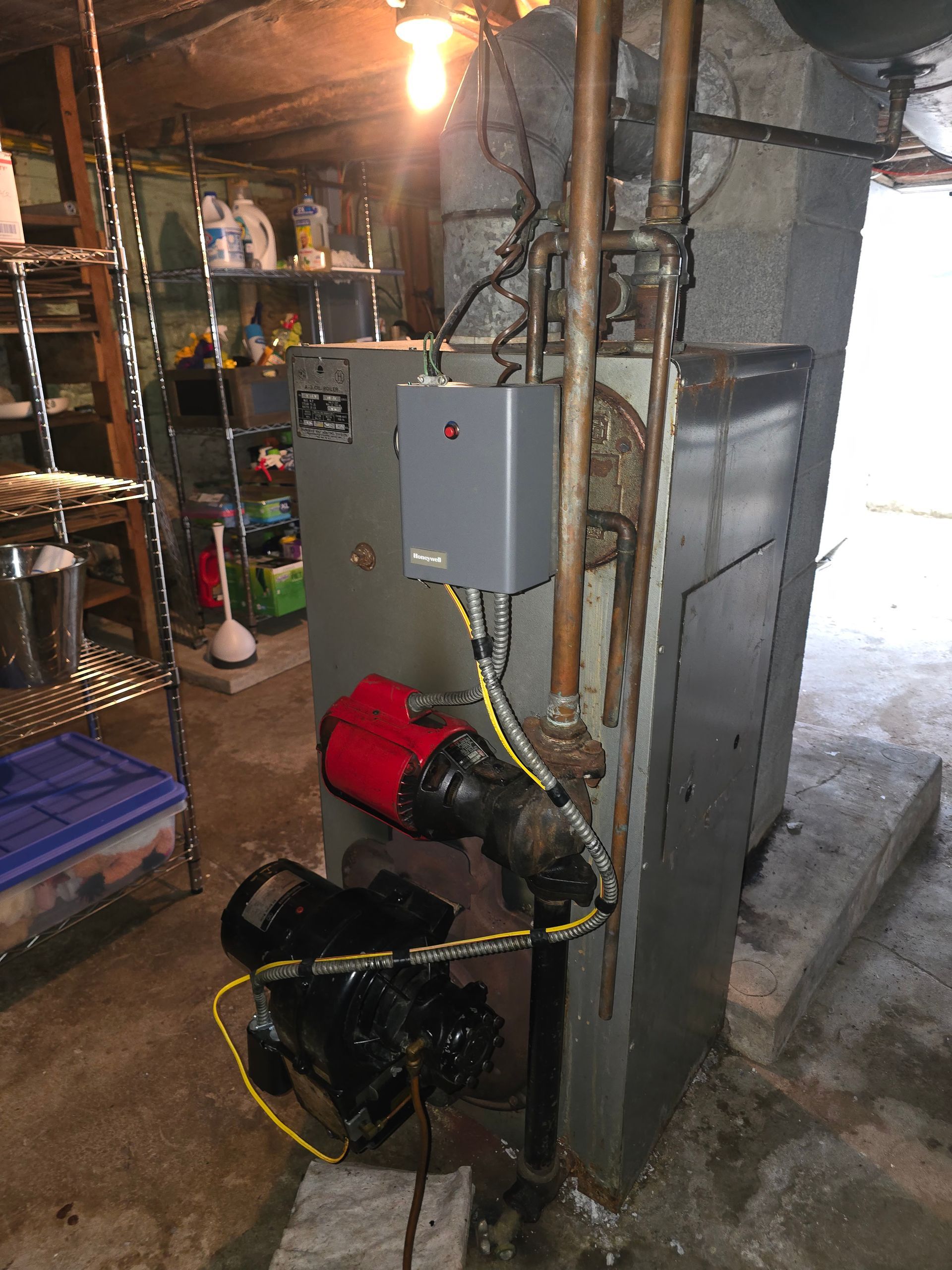 Basement utility area with exposed pipes, electrical boxes, and a red pump on the floor.