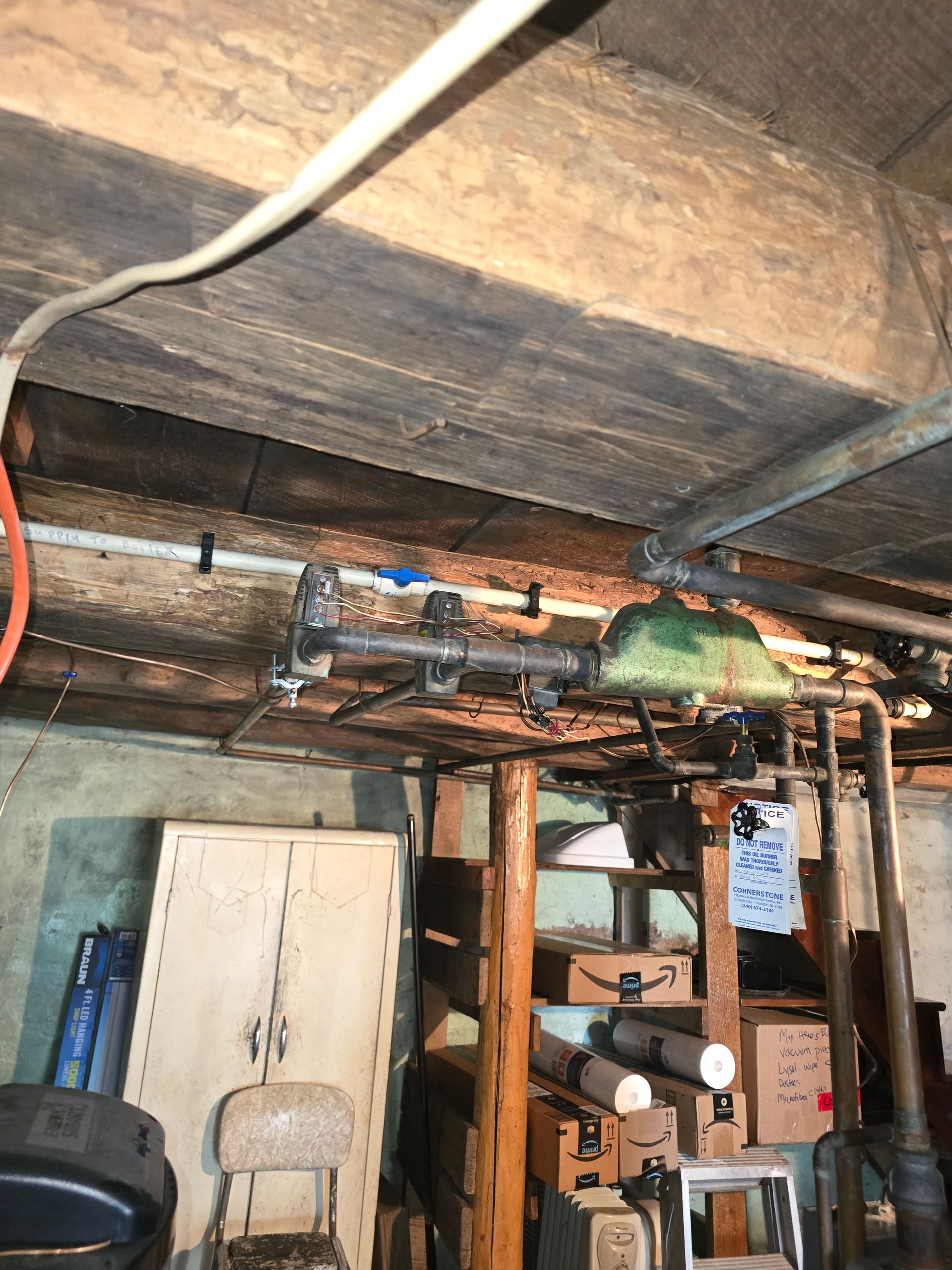 Basement utility area with exposed beams, pipes, shelves, a white cabinet, and stored tools.