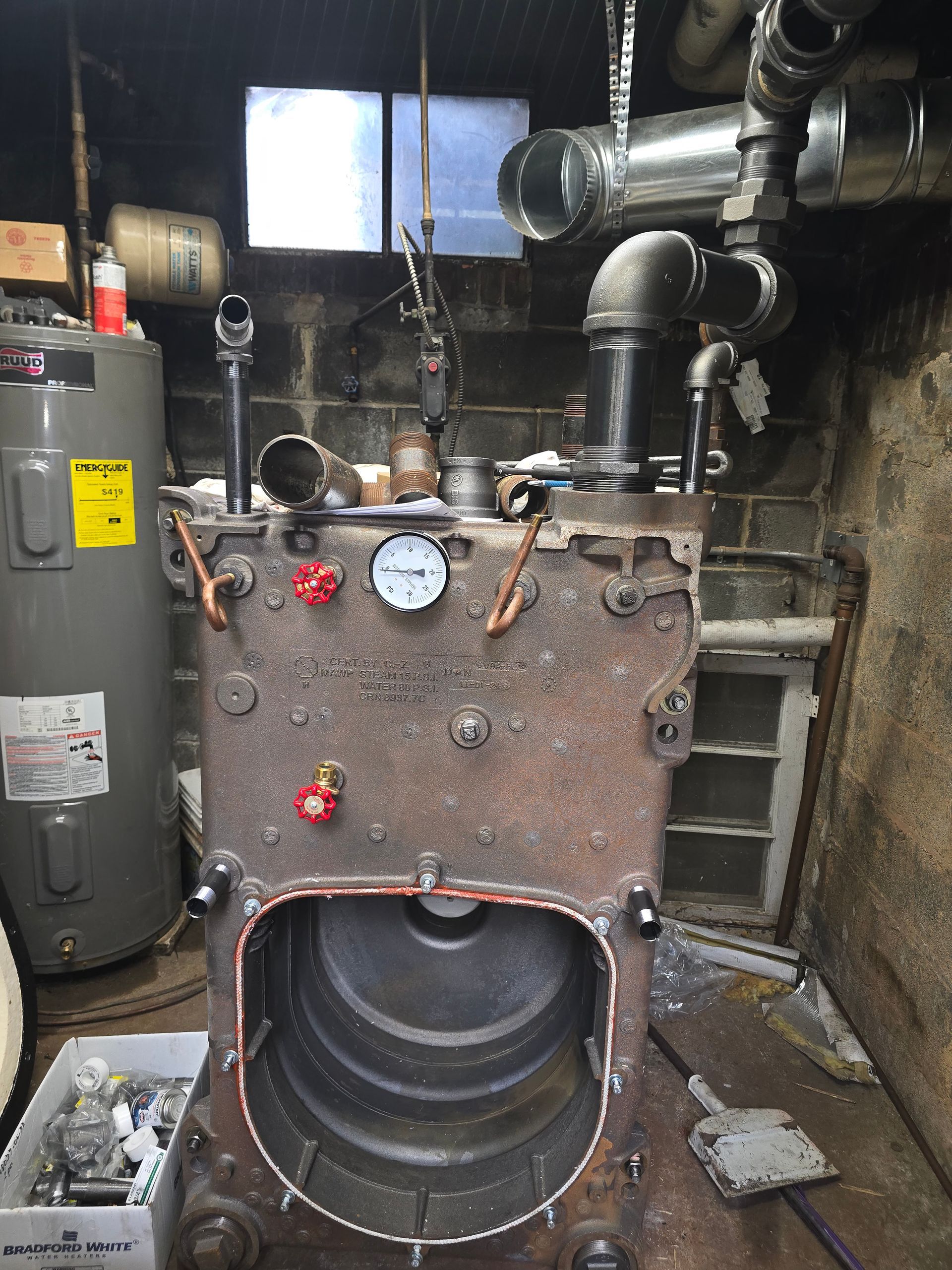 Old industrial boiler with gauges, pipes, and rust in a dim basement utility room