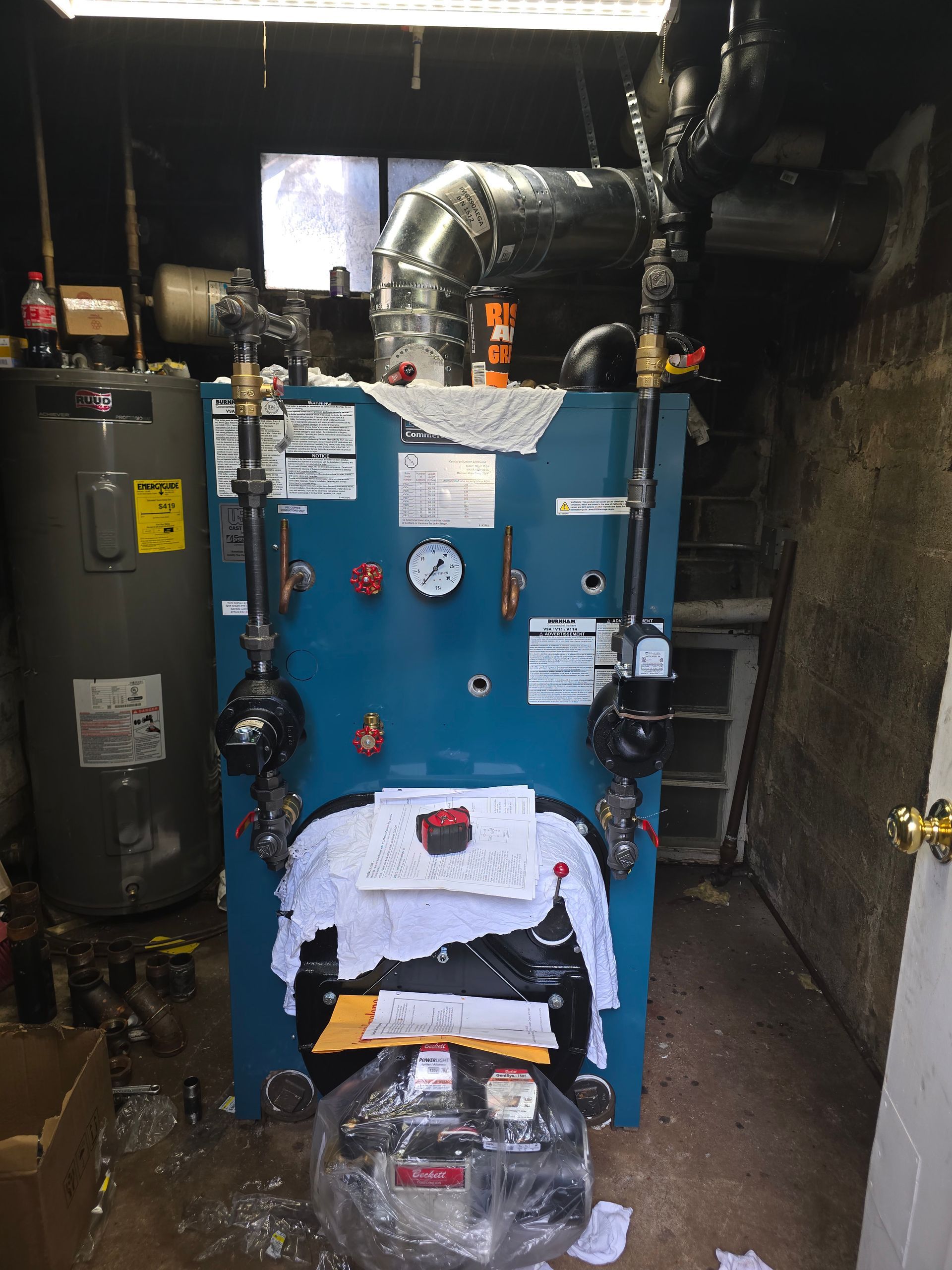 Blue furnace and boiler system in a dim basement, with ducts, pipes, and a water heater nearby