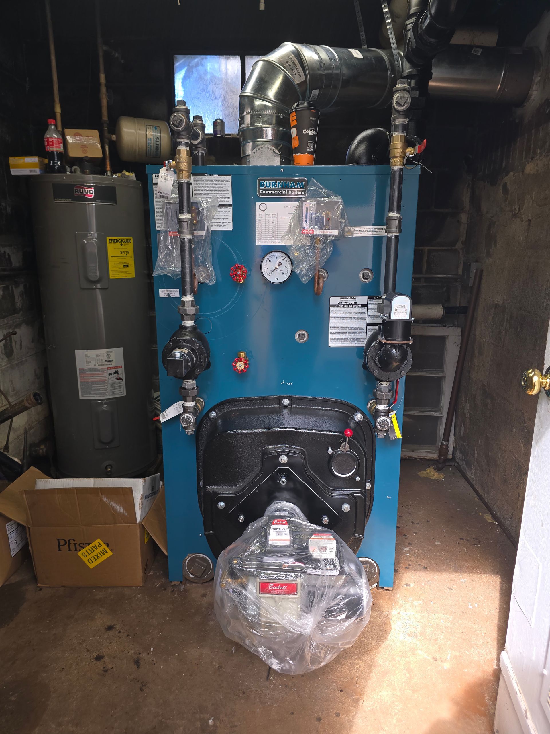 Blue industrial boiler in a basement utility room, with wrapped equipment and pipes around it.