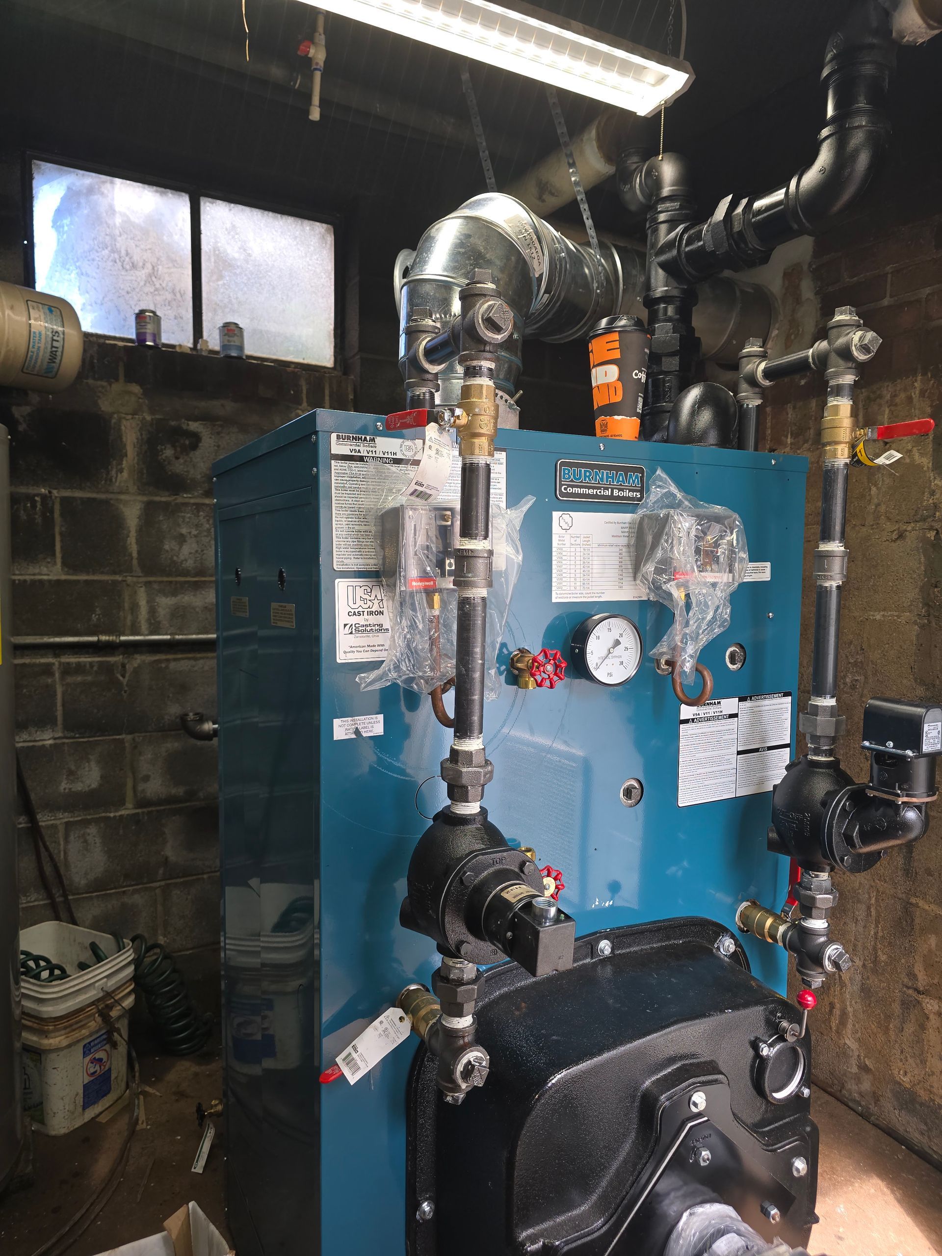 Blue industrial boiler with pipes and ductwork in a dim basement utility room