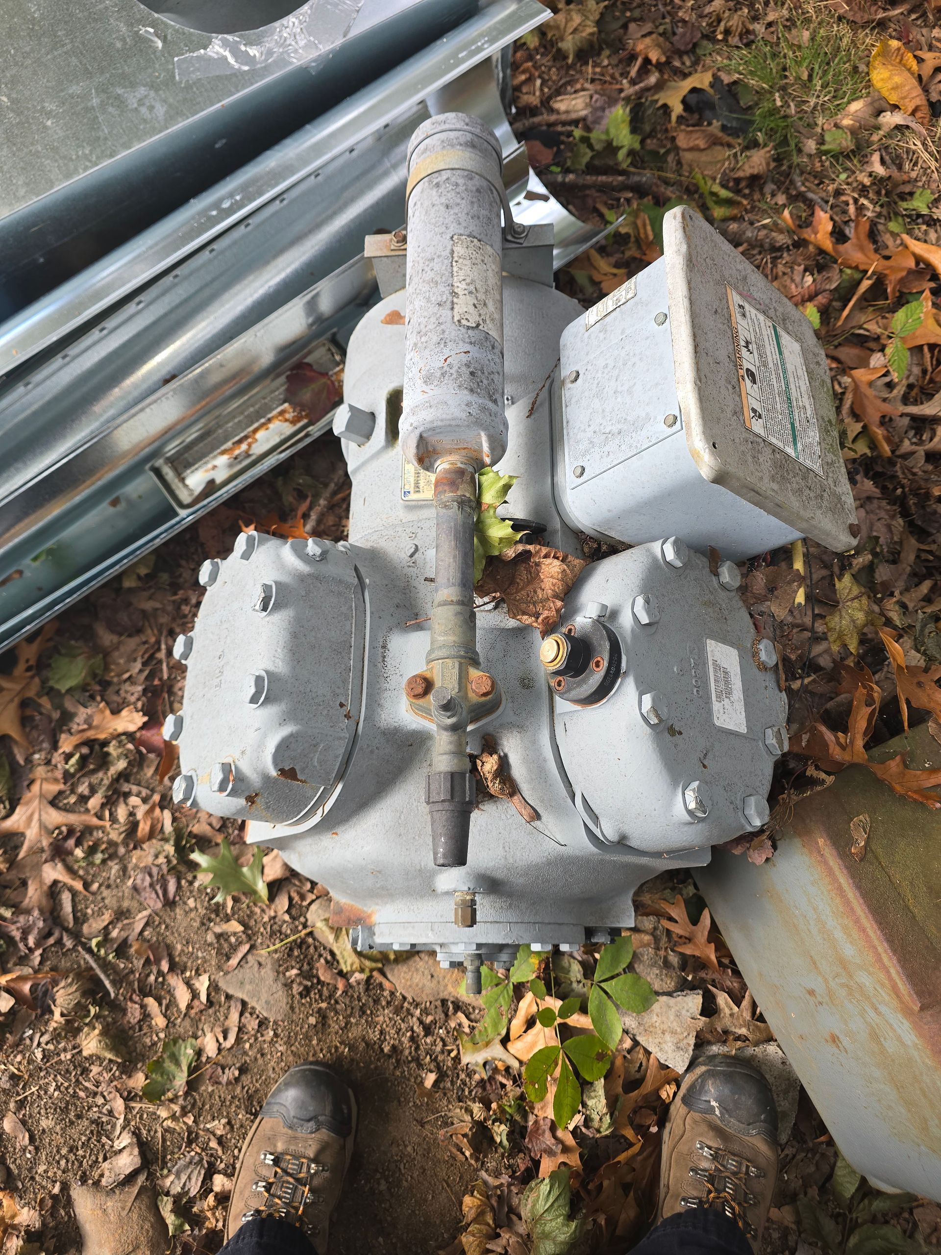 Gray gas valves and piping beside a metal guardrail, covered in dirt and leaves outdoors