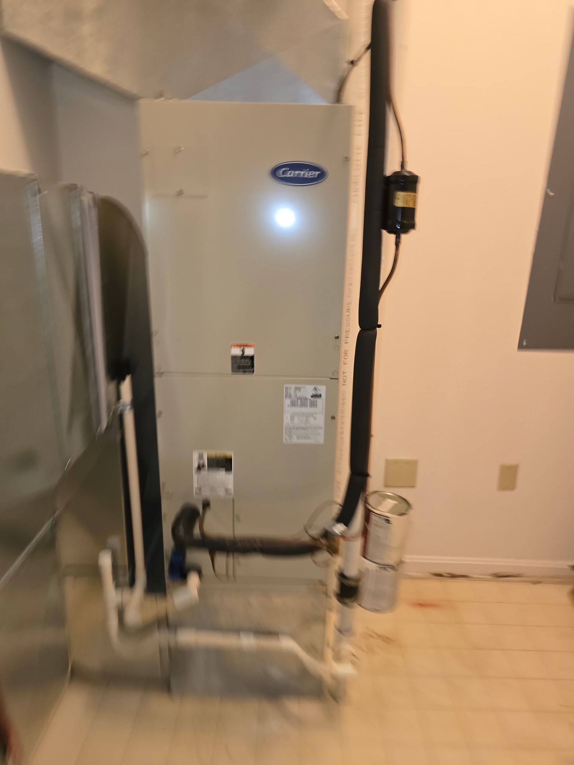 Air handler in a utility room beside exposed piping and a tiled floor.