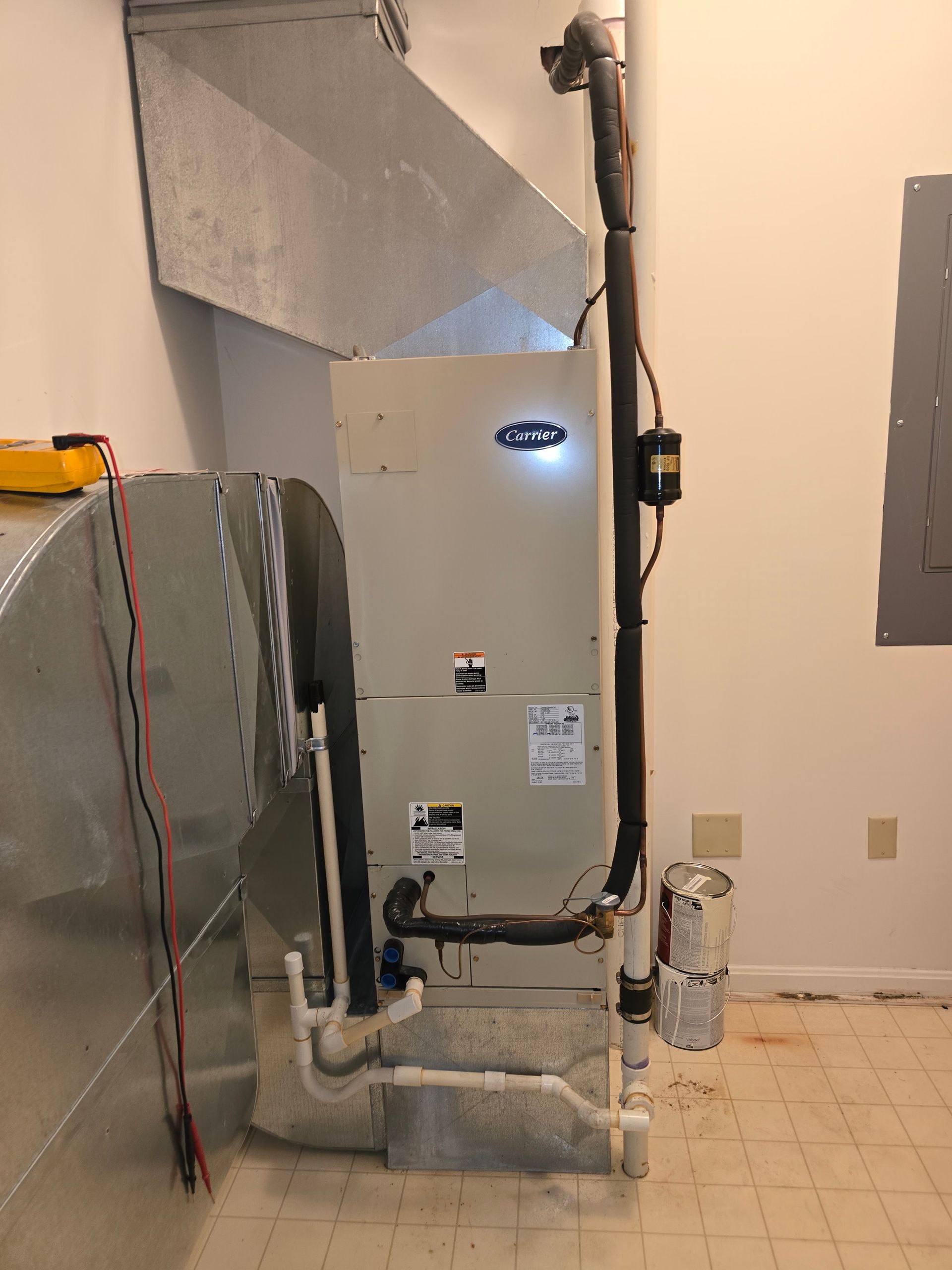 Large HVAC unit in a basement/utility room with ductwork, pipes, and a tiled floor.
