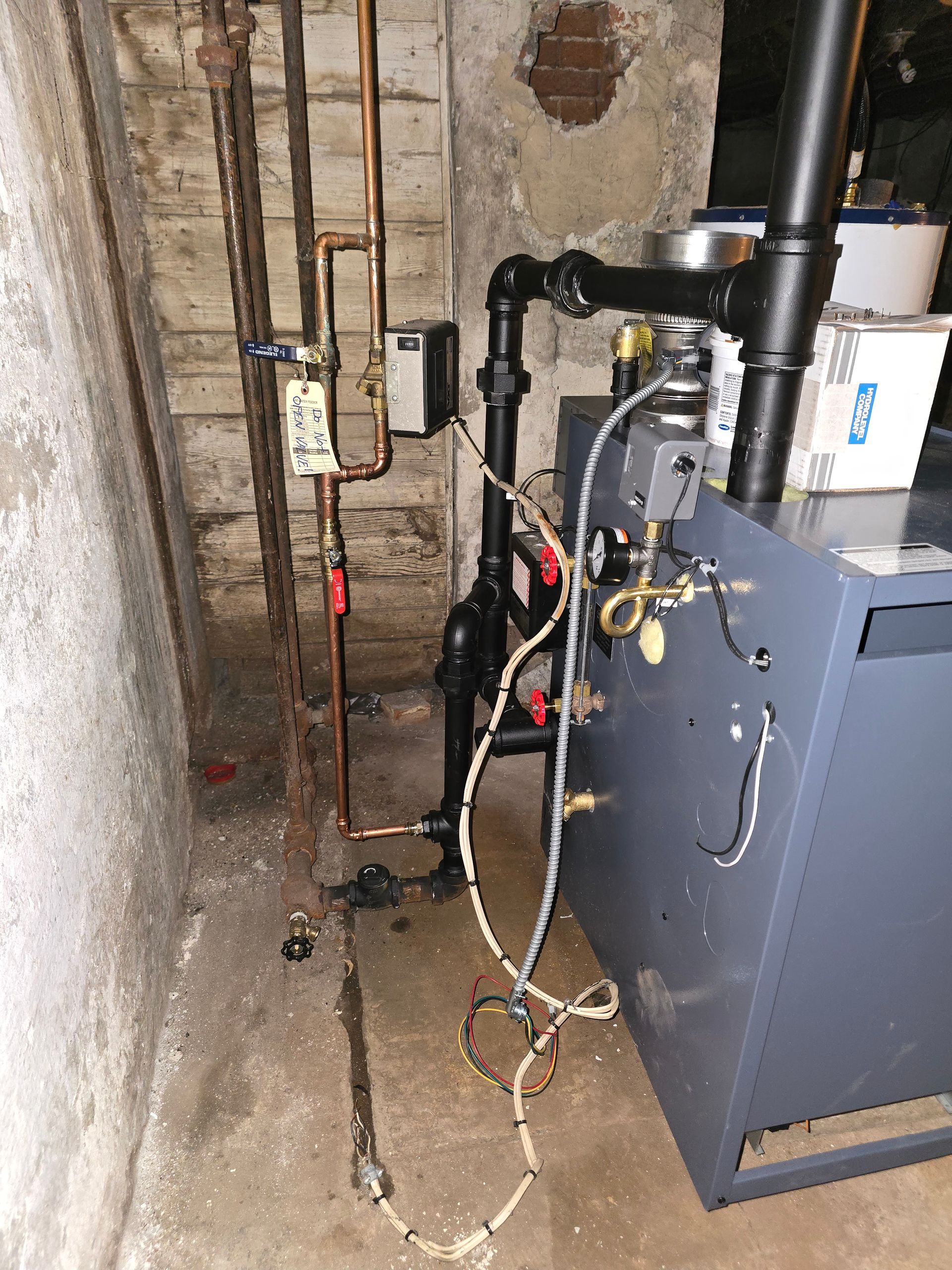 Basement boiler with exposed pipes and valves against a concrete wall.