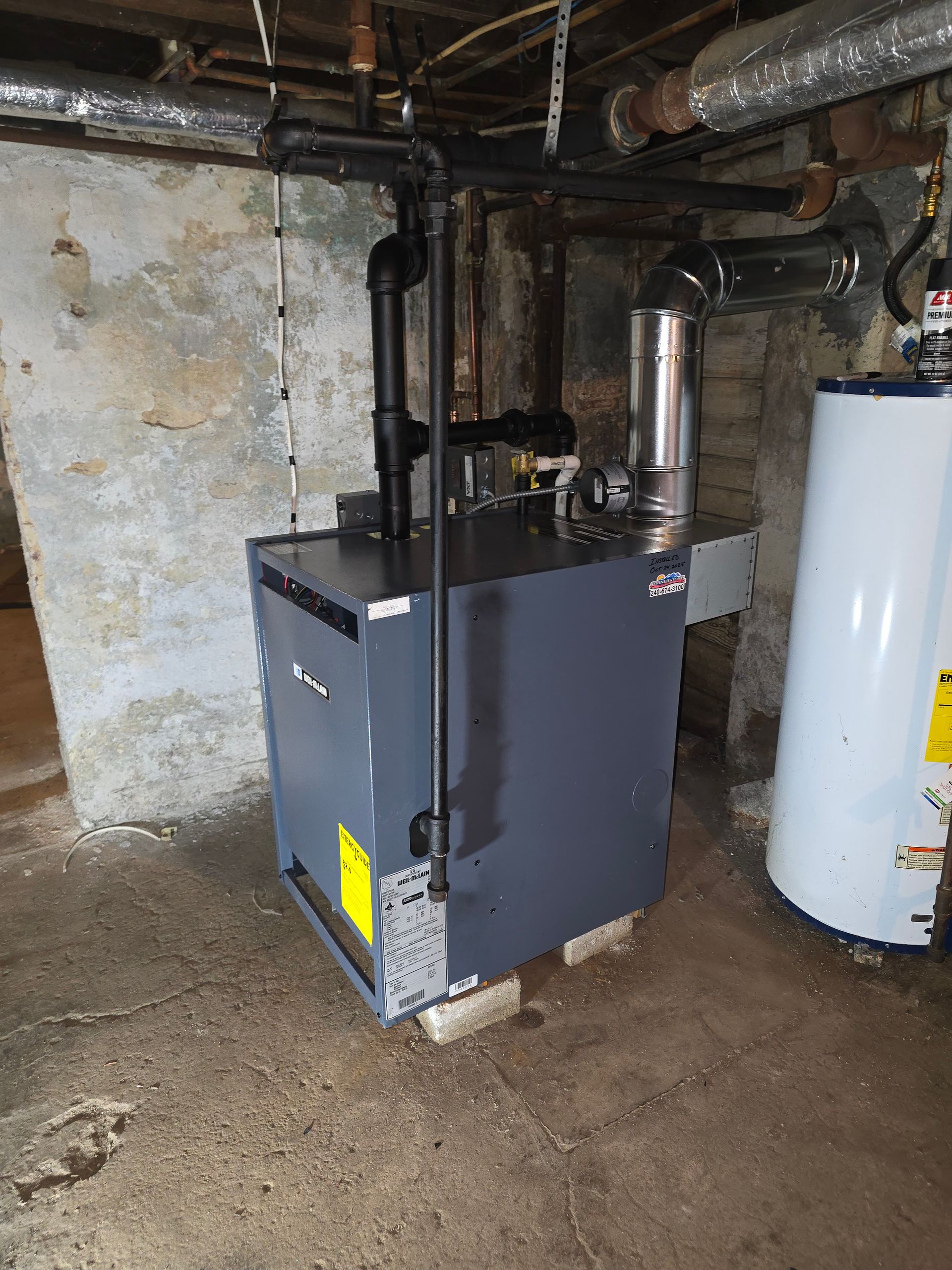 Gray furnace in a basement beside a white water heater and exposed pipes.