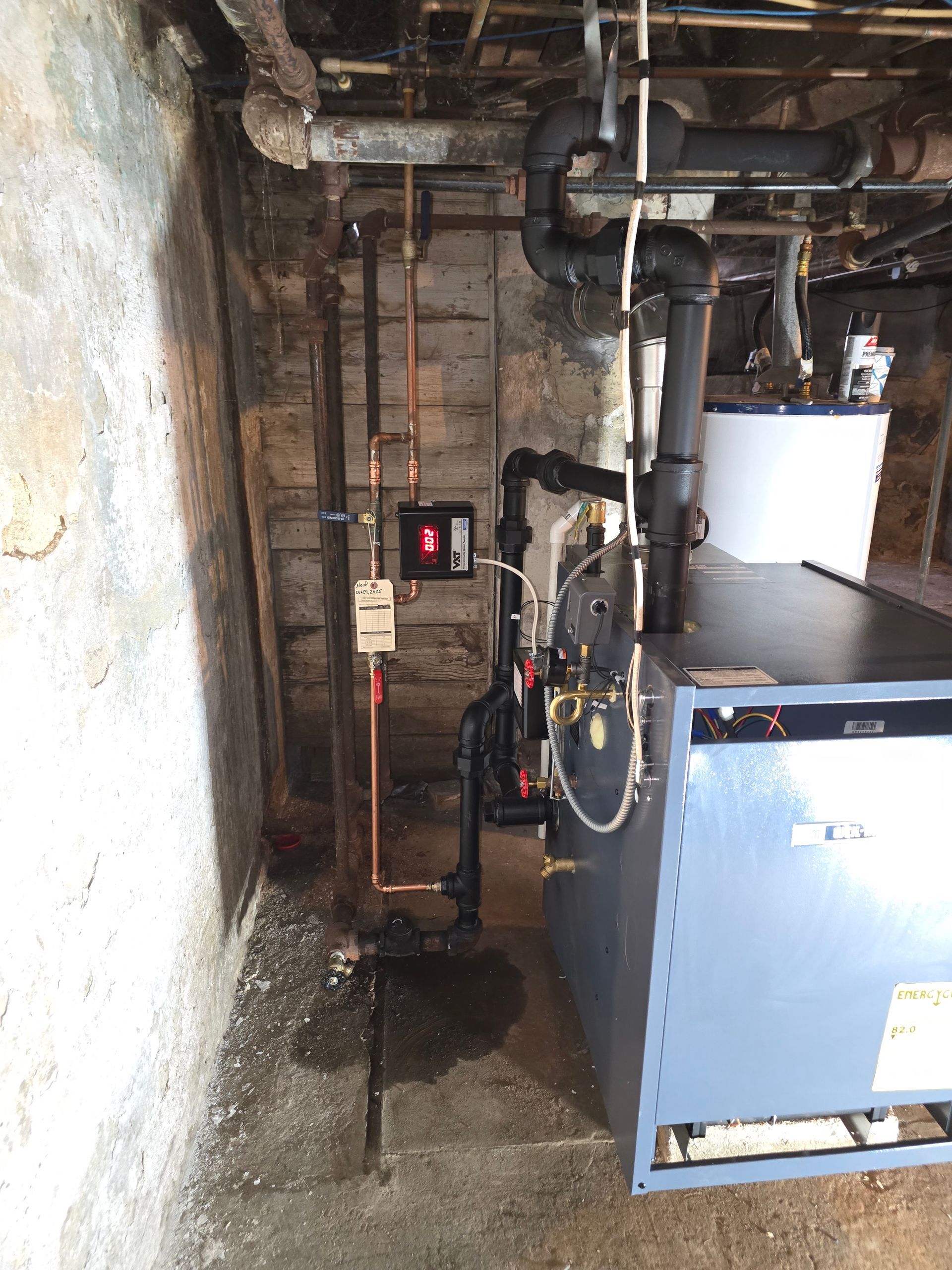 Utility room with pipes, pumps, and a blue boiler against a rough concrete wall.