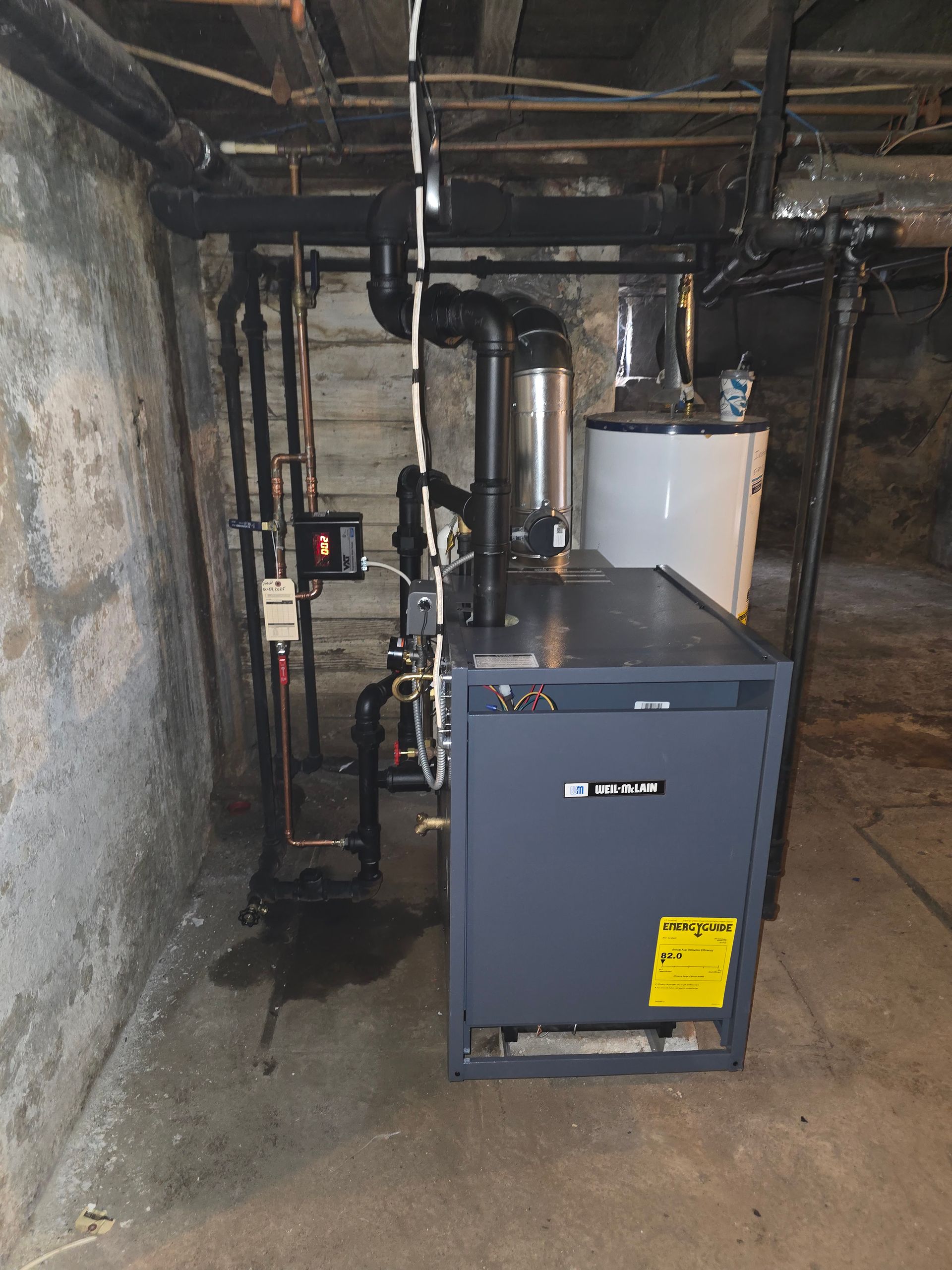 Basement utility room with a gray boiler, white water heater, and exposed pipes.
