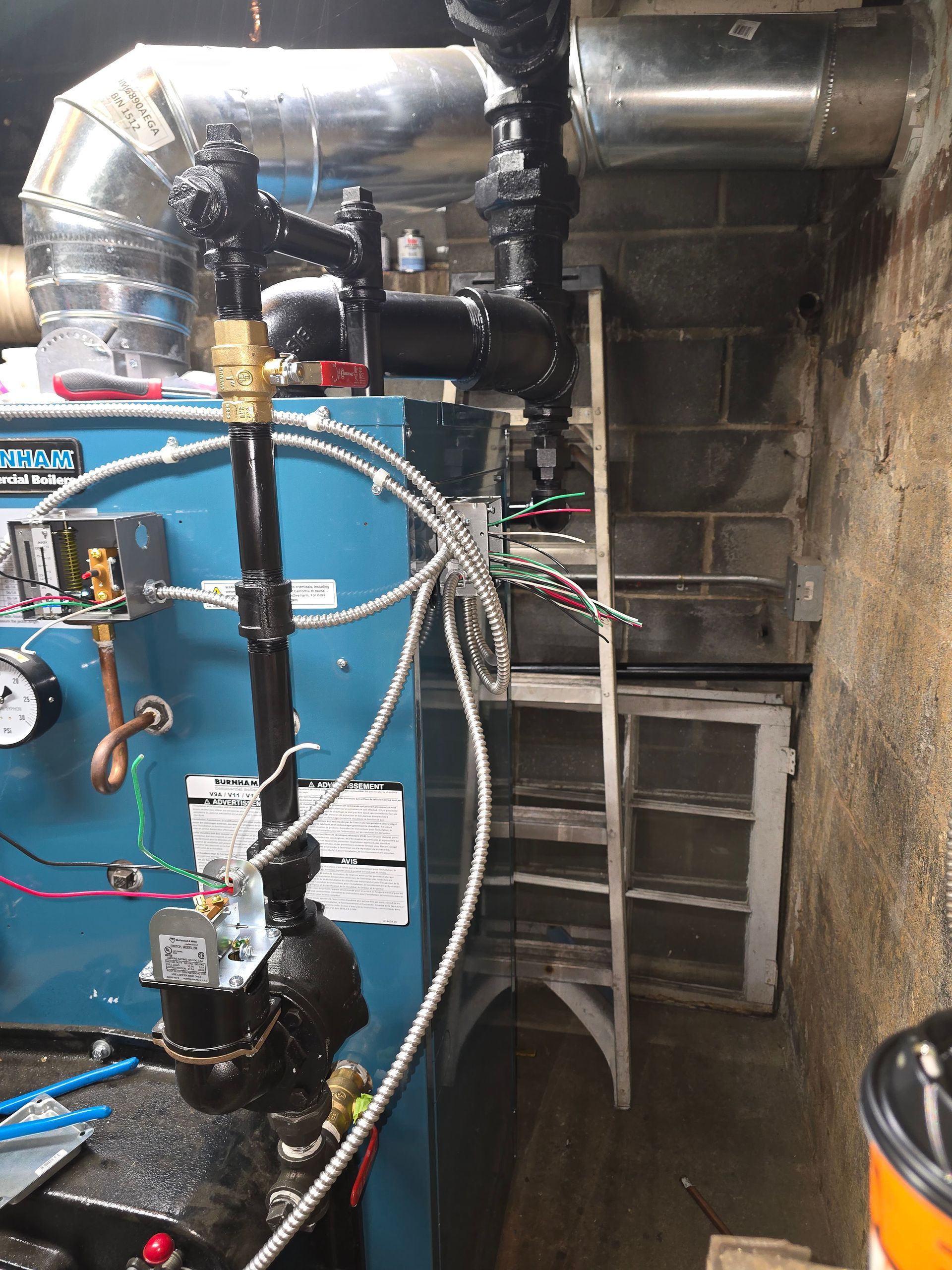 Industrial boiler room with blue boiler, silver ducts, pipes, and a metal ladder in a dim utility space