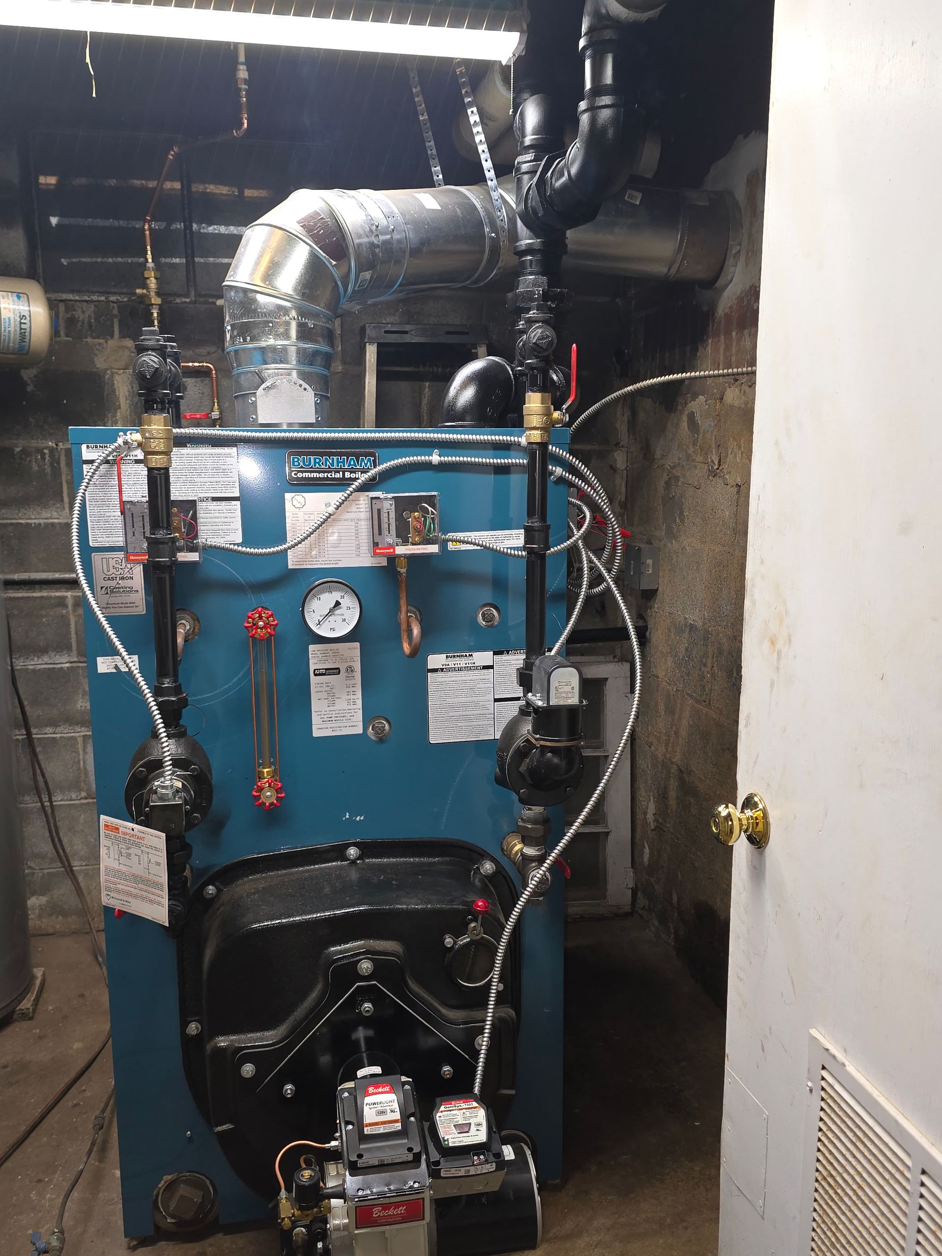 Blue industrial boiler with pipes and gauges in a cramped utility room