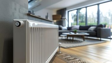 White radiator in a bright modern living room with sofa, coffee table, and large window.