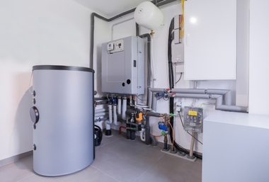 Utility room with water heater, boiler, pipes, and wall-mounted equipment in a clean basement.