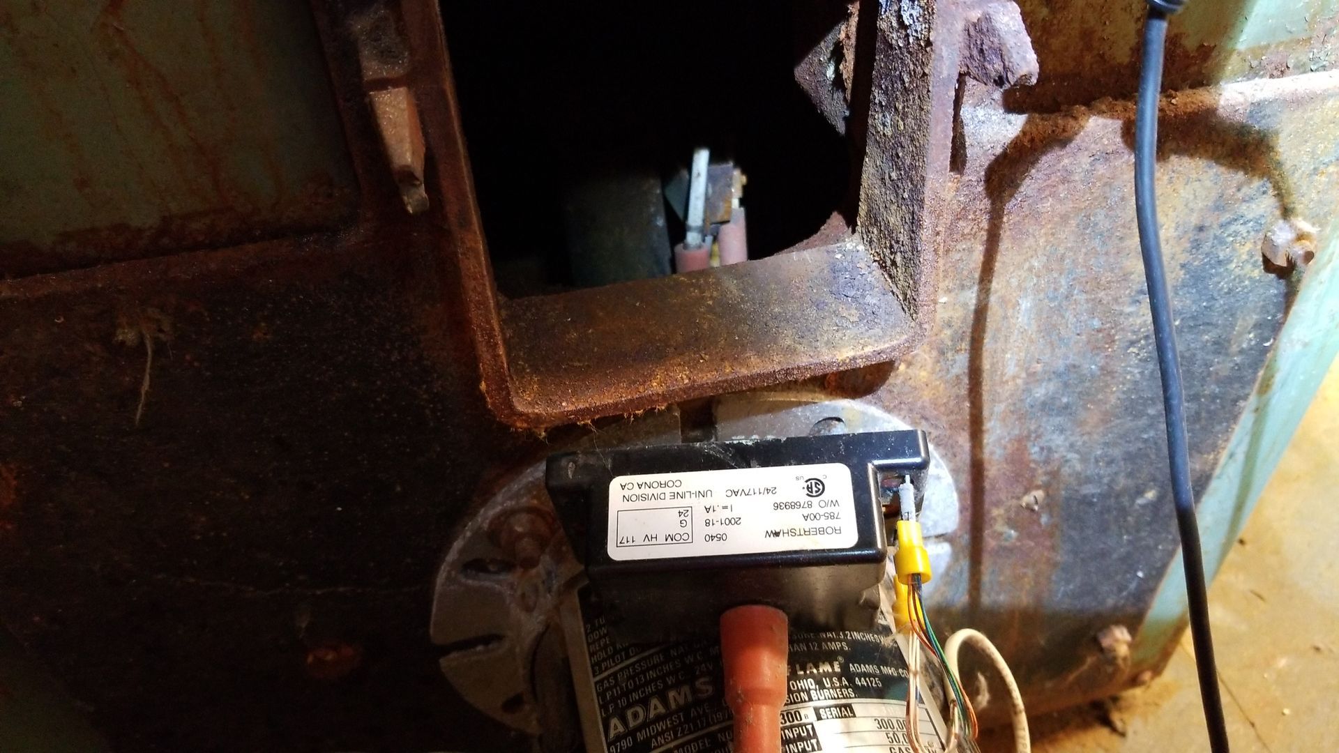 Industrial machinery motor with orange hoses beside a rusted blue metal tank