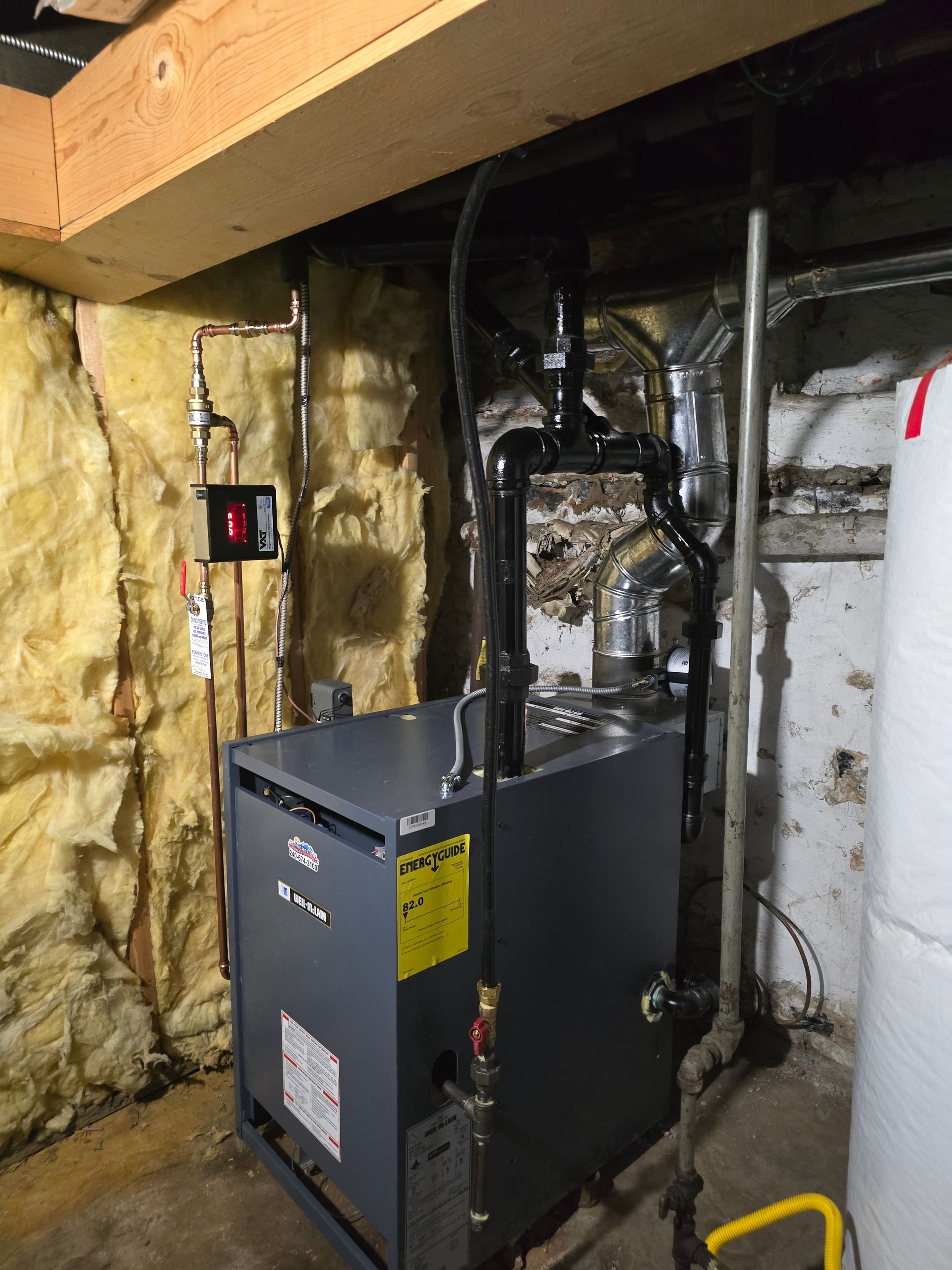 Black furnace and ductwork in unfinished basement with exposed insulation and pipes