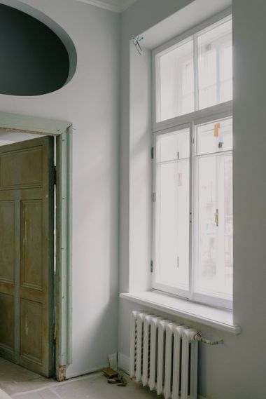 Empty room with a tall white window, radiator below, and an open wooden door on the left.