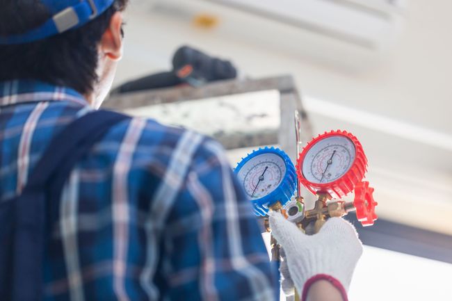Technician holding red and blue manifold gauges while servicing an HVAC unit indoors