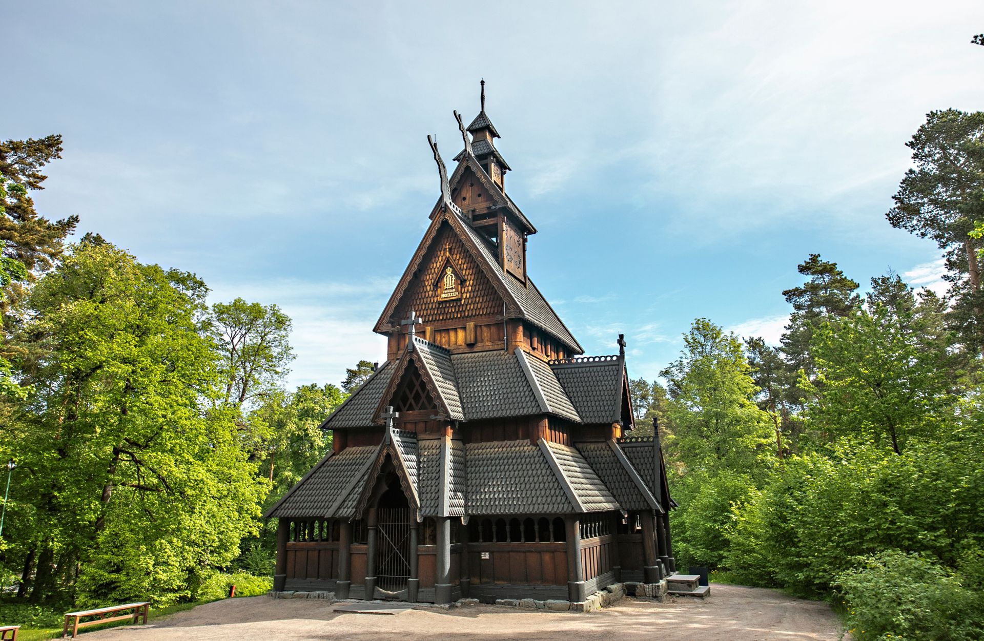 En stavkirke av tre med et lagdelt tak av shingel, plassert i en frodig grønn skogslysning.