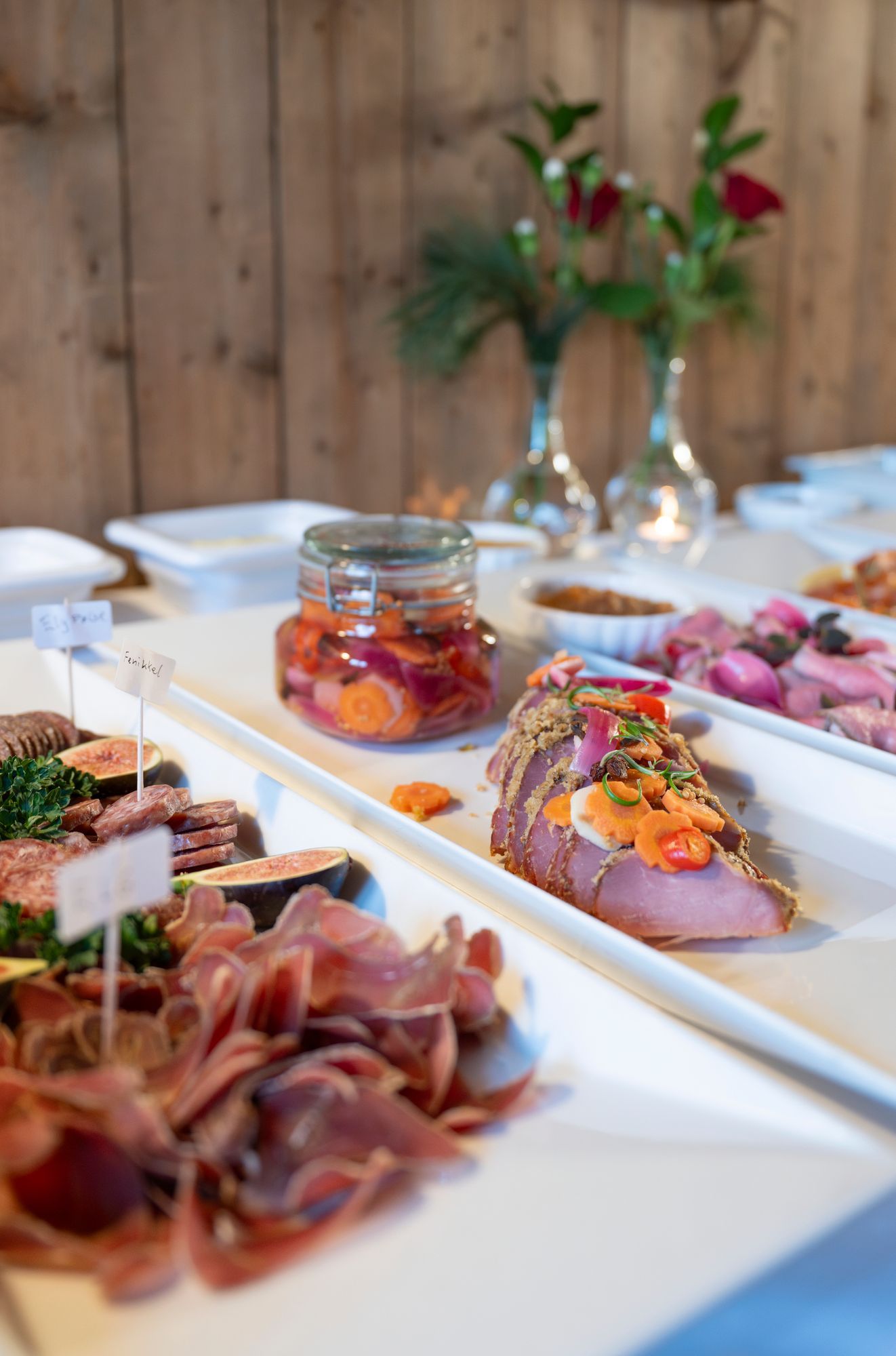 Et buffébord med lange hvite fat med skiver av spekemat, fiken, et glass med syltede grønnsaker