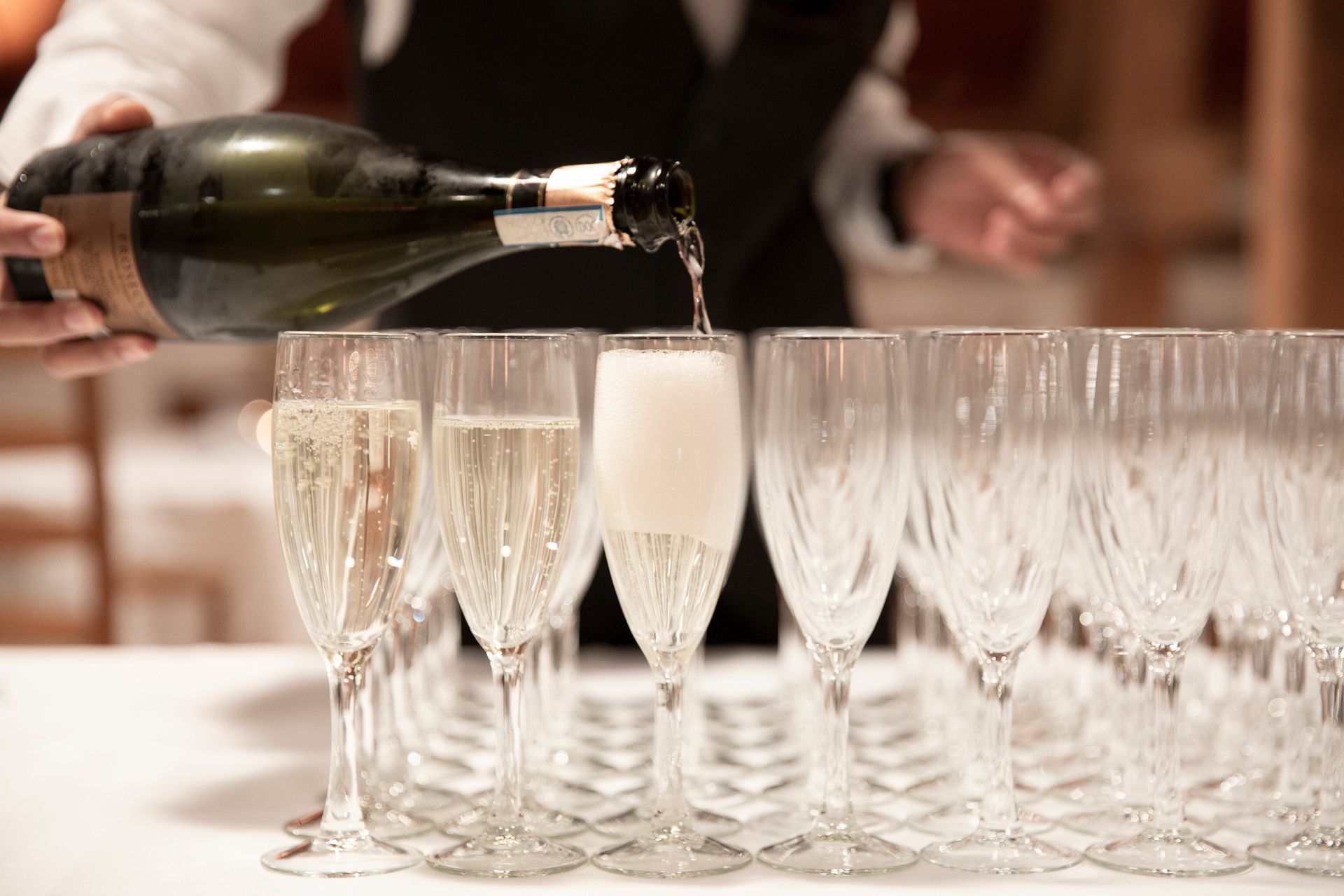 En servitør heller champagne i en rad med glass med stilk.
