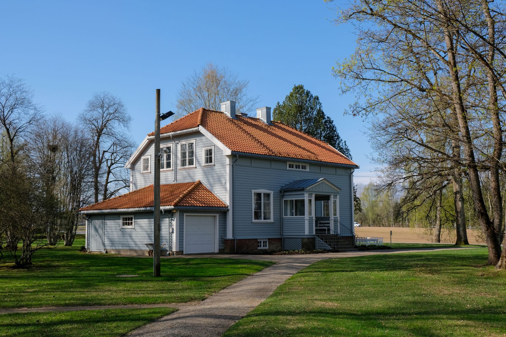 Blått hus med oransje tegltak, garasje og gangvei på grønn plen, under blå himmel.