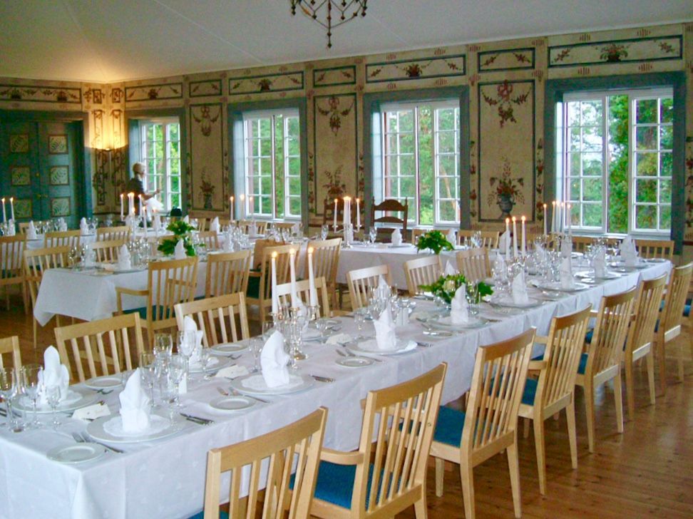 En mykt opplyst, elegant spisestue med runde bord, hvite duker og dekket med stearinlys til en formell begivenhet.