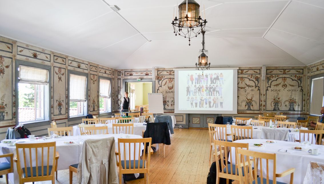 Elegant spisestue med runde bord, hvite duker, blomstertapet og et projektorlerret foran