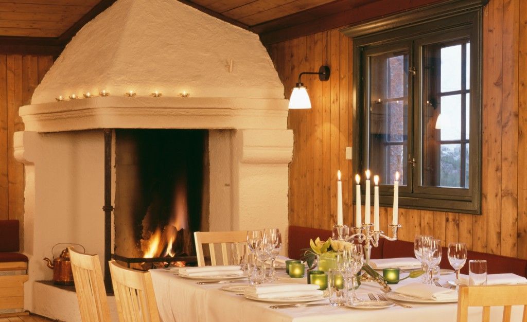 Koselig rustikk spisestue med tent peis, dekket bord og stearinlys ved et vindu