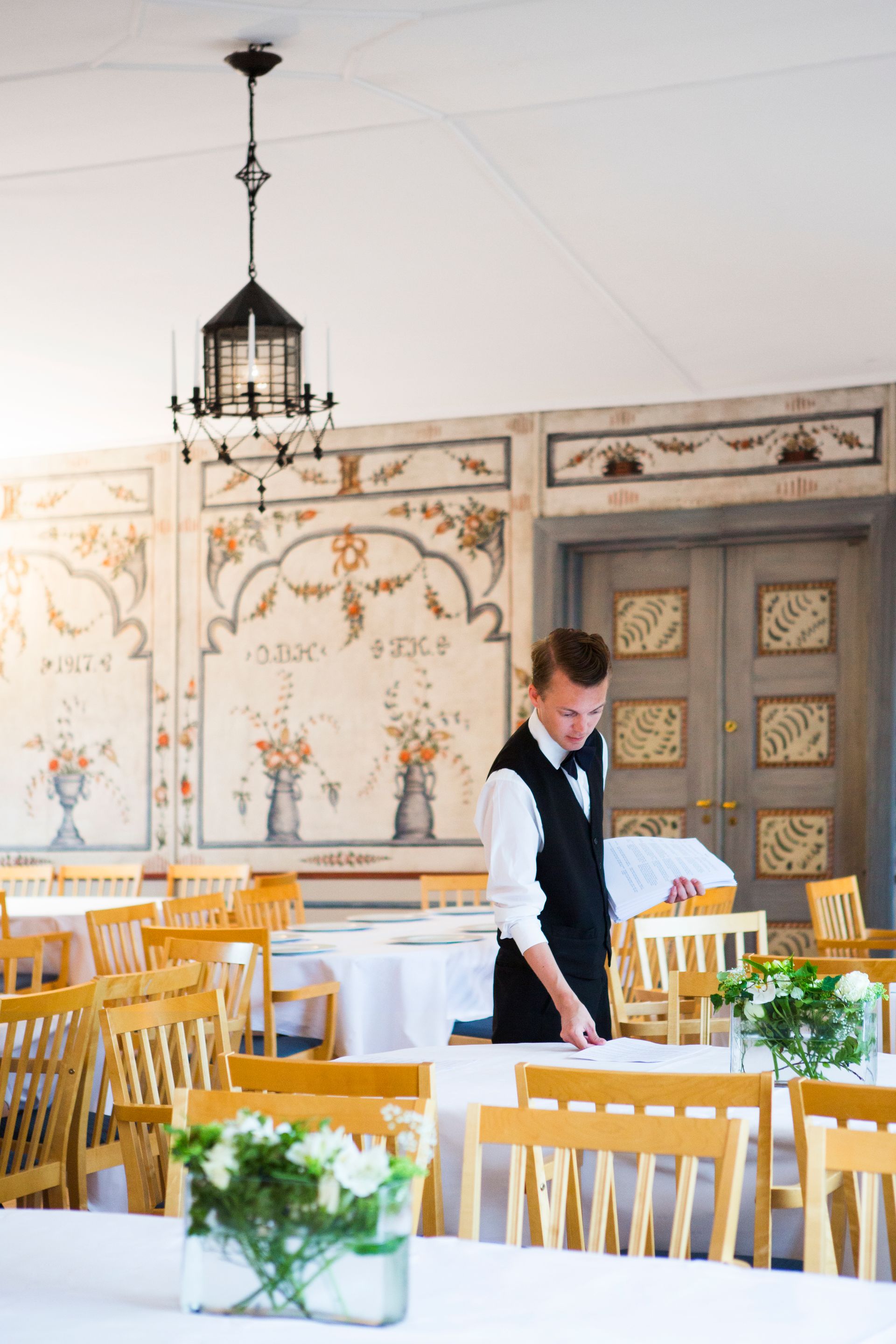Kelner dekker bord i en lys, elegant spisesal med hvite og gule stoler