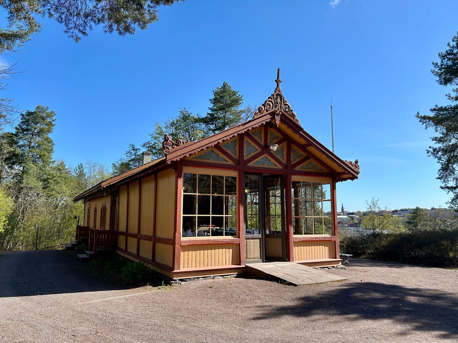 Trepaviljong med glassvinduer og utsmykket tak, plassert i en park på en solrik dag.