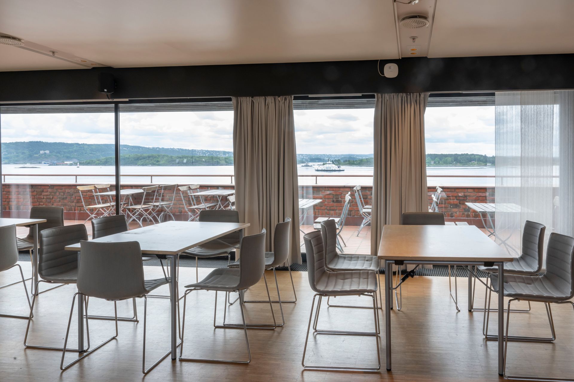 Spisestue med bord og stoler i nærheten av store vinduer med utsikt over et vann og fjerntliggende land.
