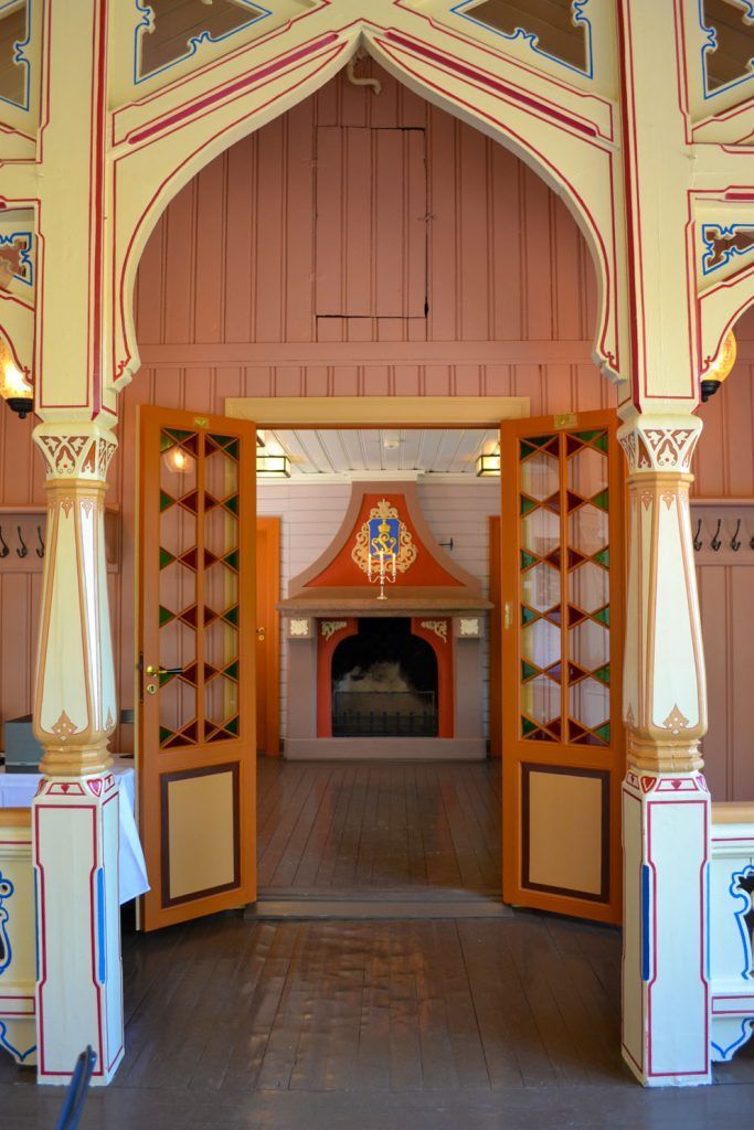 En døråpning med dekorative tresøyler som rammer inn en åpen inngang til et rom med peis og fargerike veggdetaljer.