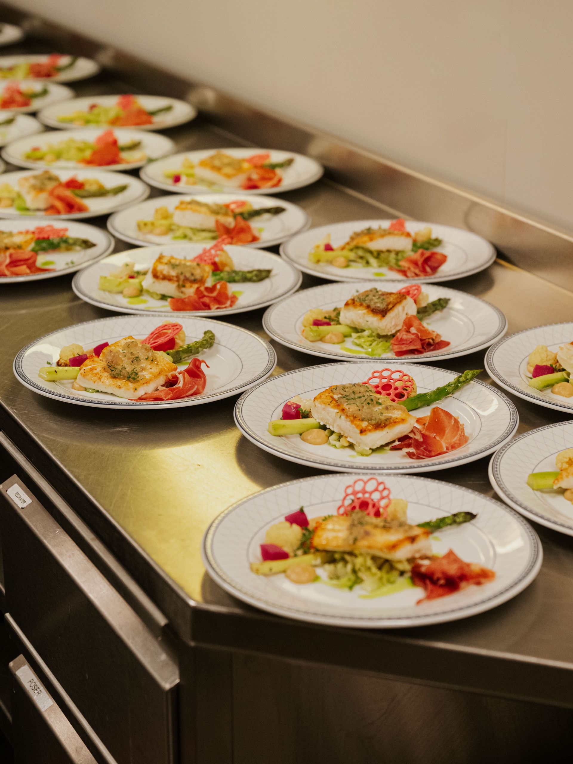 Plates of plated salads lined up on a stainless-steel counter in a kitchen.